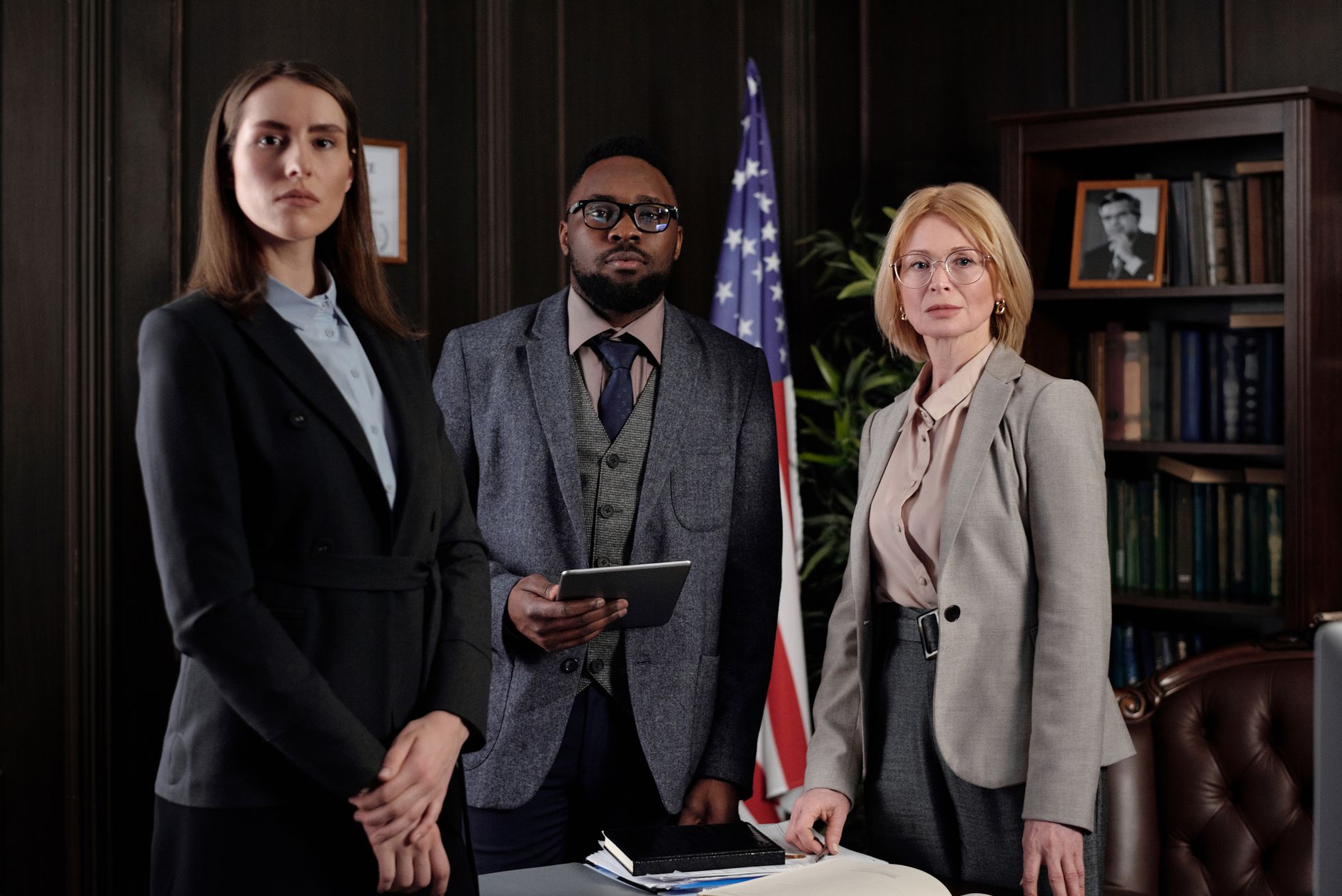 A diverse group of professionals in a formal office setting featuring an American flag and bookshelves.