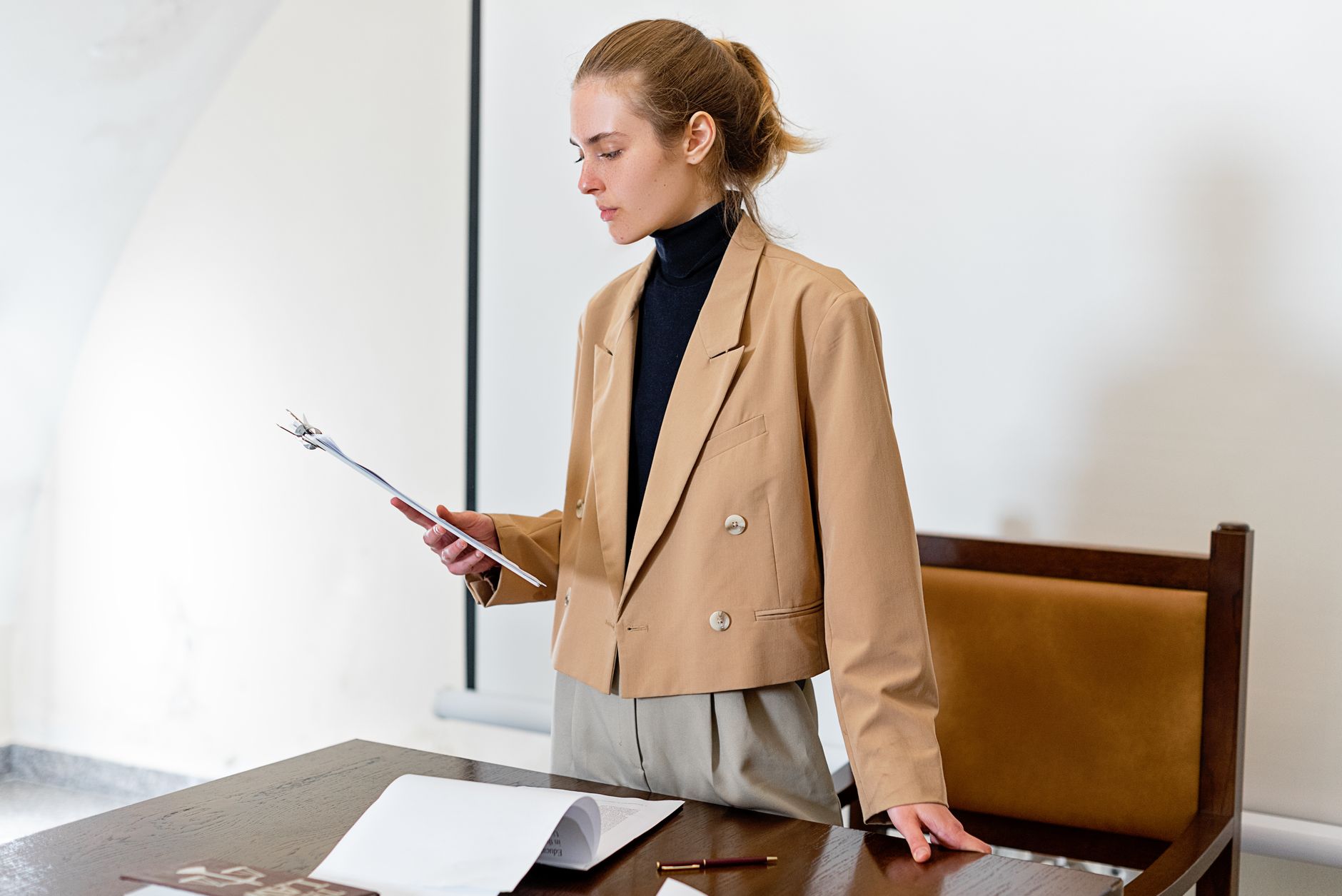 Caucasian woman in business attire evaluating a document in an indoor office setting.