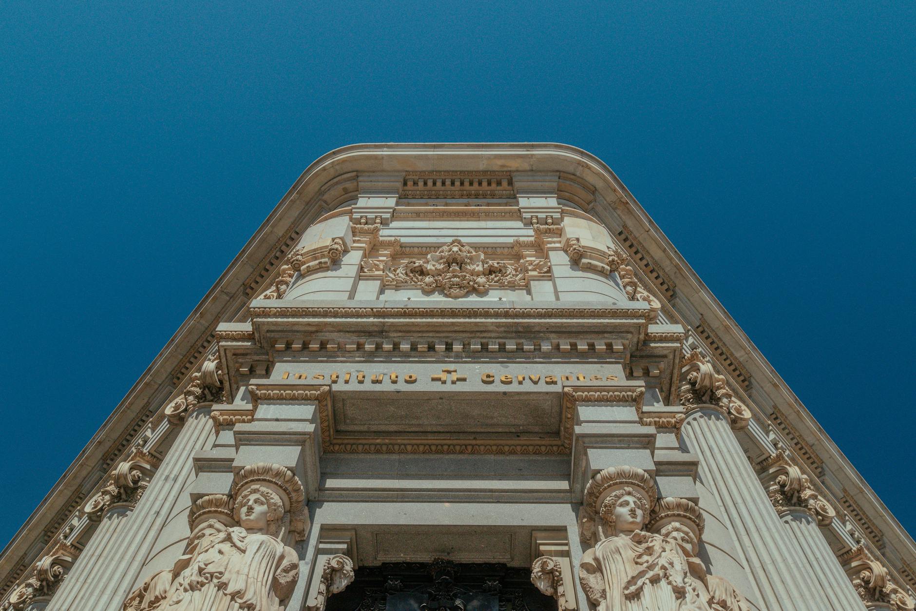 Ornate architecture of Instituto Cervantes with sculptures, set against a clear blue sky.