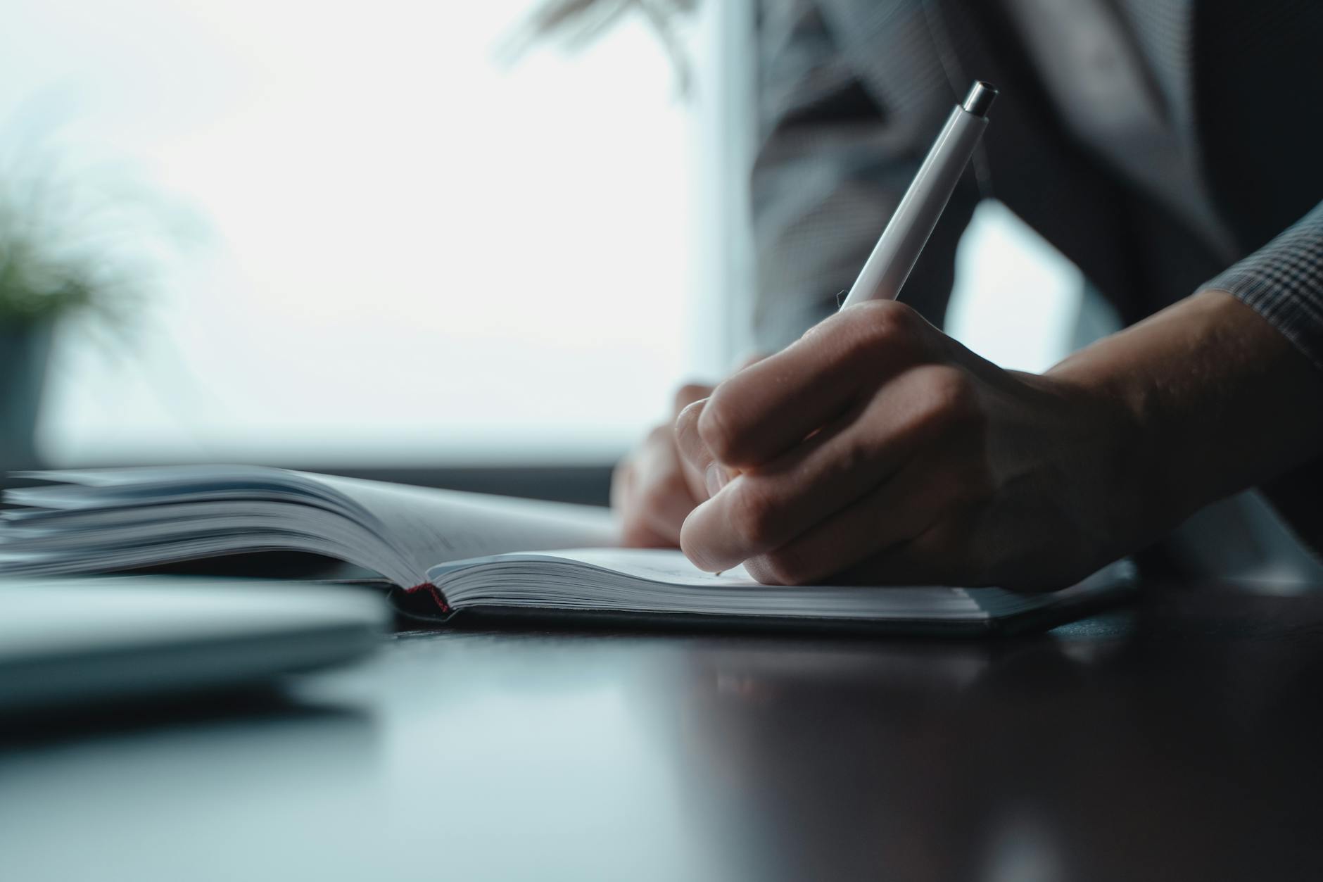 A person writing in a notebook with a pen, focusing on the hand and paper.