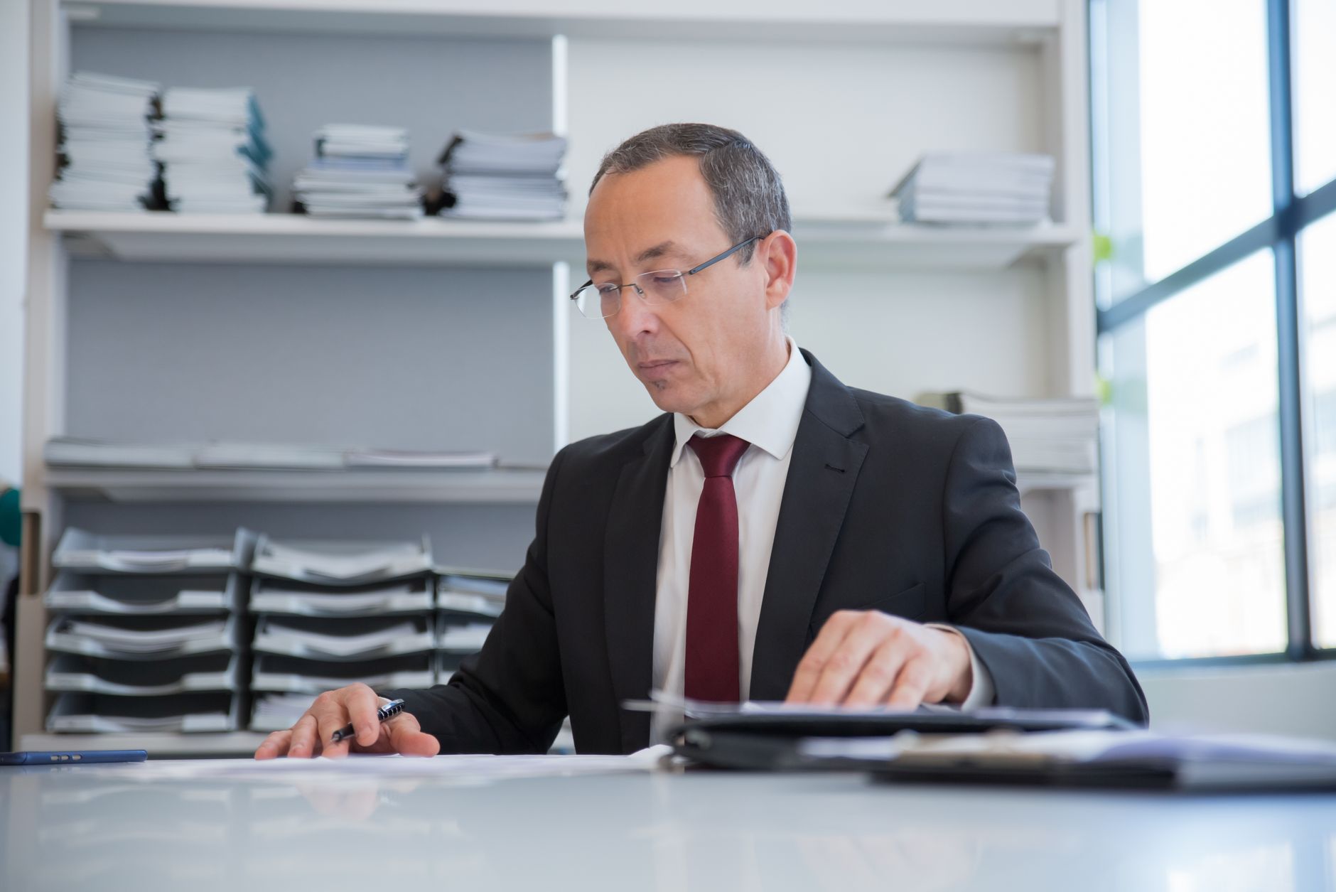 Businessman in a formal setting reviewing documents at an office desk.