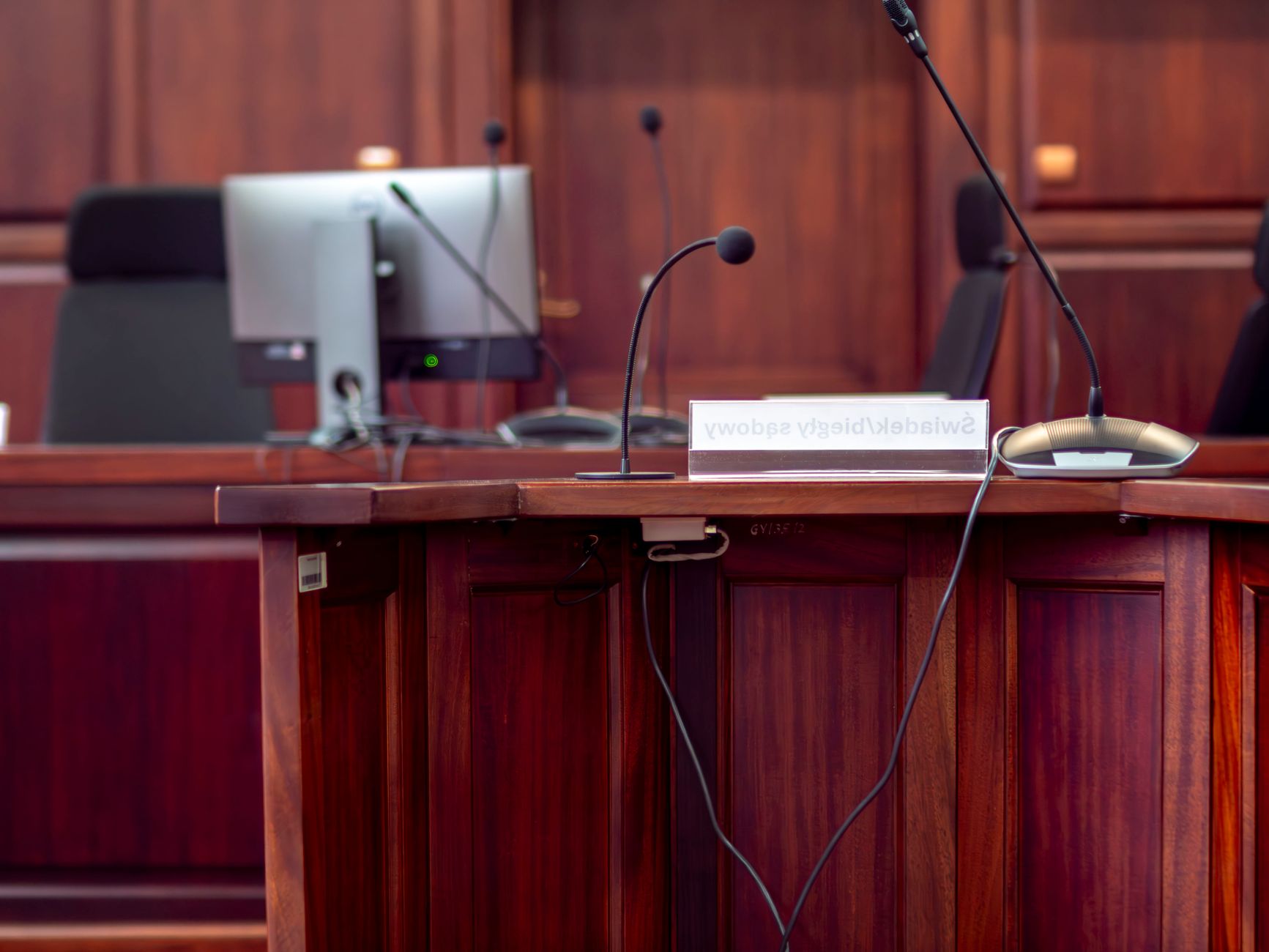 Close-up of a wooden podium with microphones in a Polish courtroom setting.