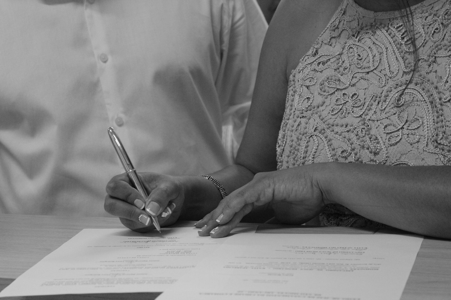 Black and white image of a couple signing documents, focusing on their hands and pen.