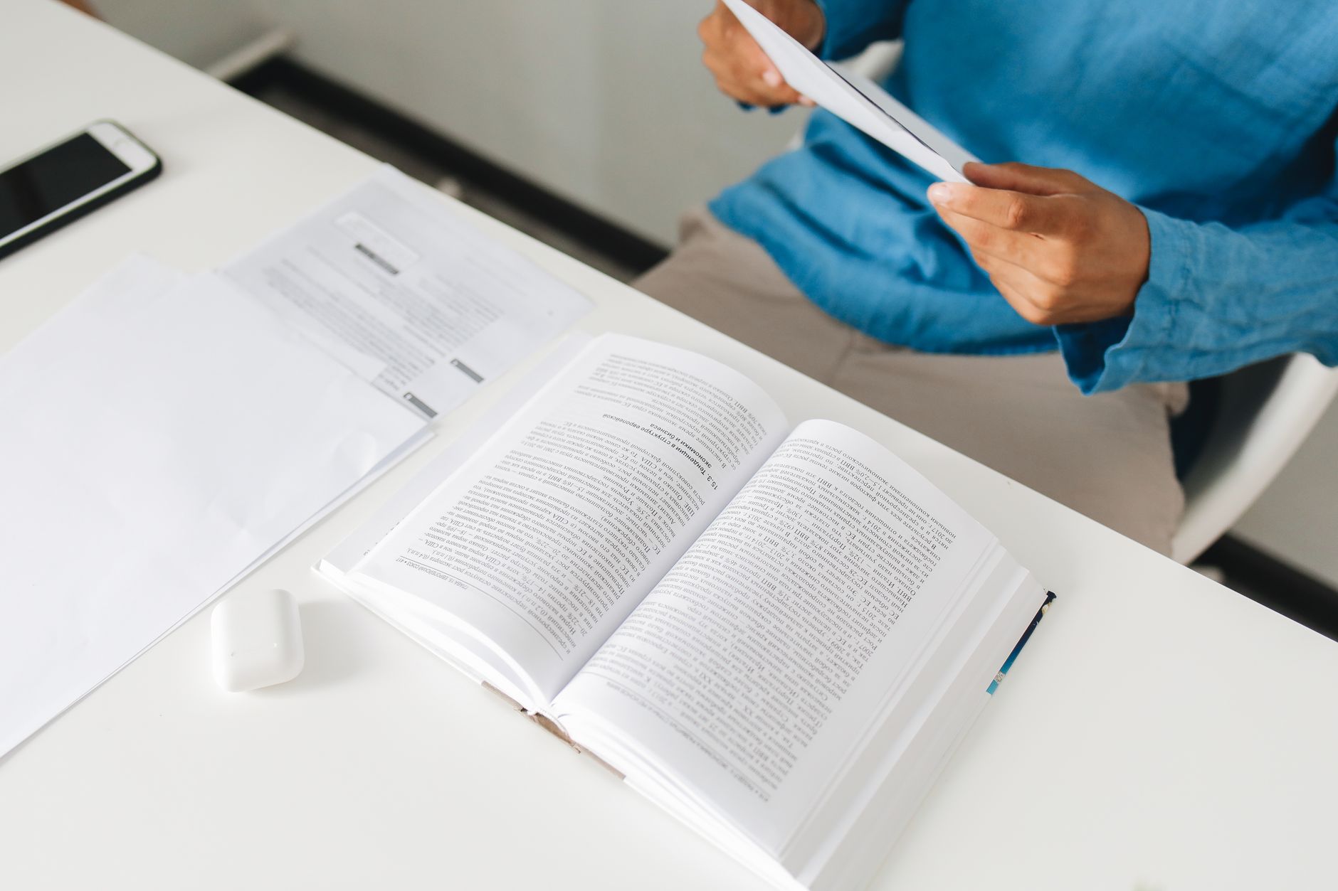 An open book on a desk with a person reading documents beside it in an office setting.