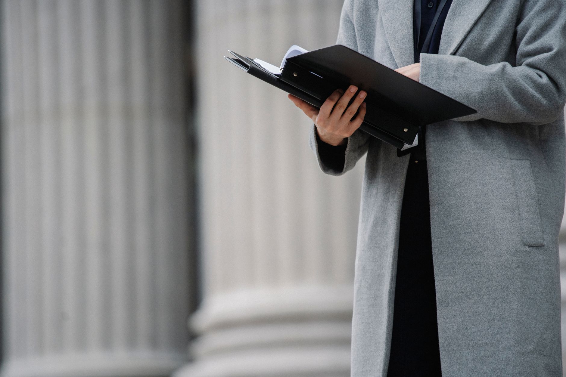 Crop unrecognizable businesswoman in gray coat standing on street with opened document folder and reading contract on autumn day