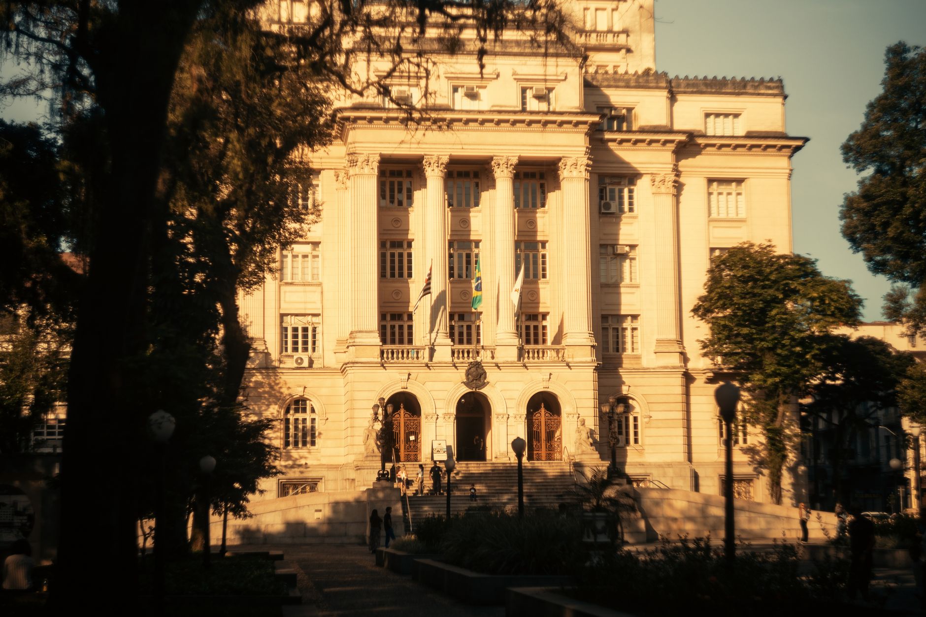 Elegant historic building facade illuminated by warm sunlight, featuring columns and flags.