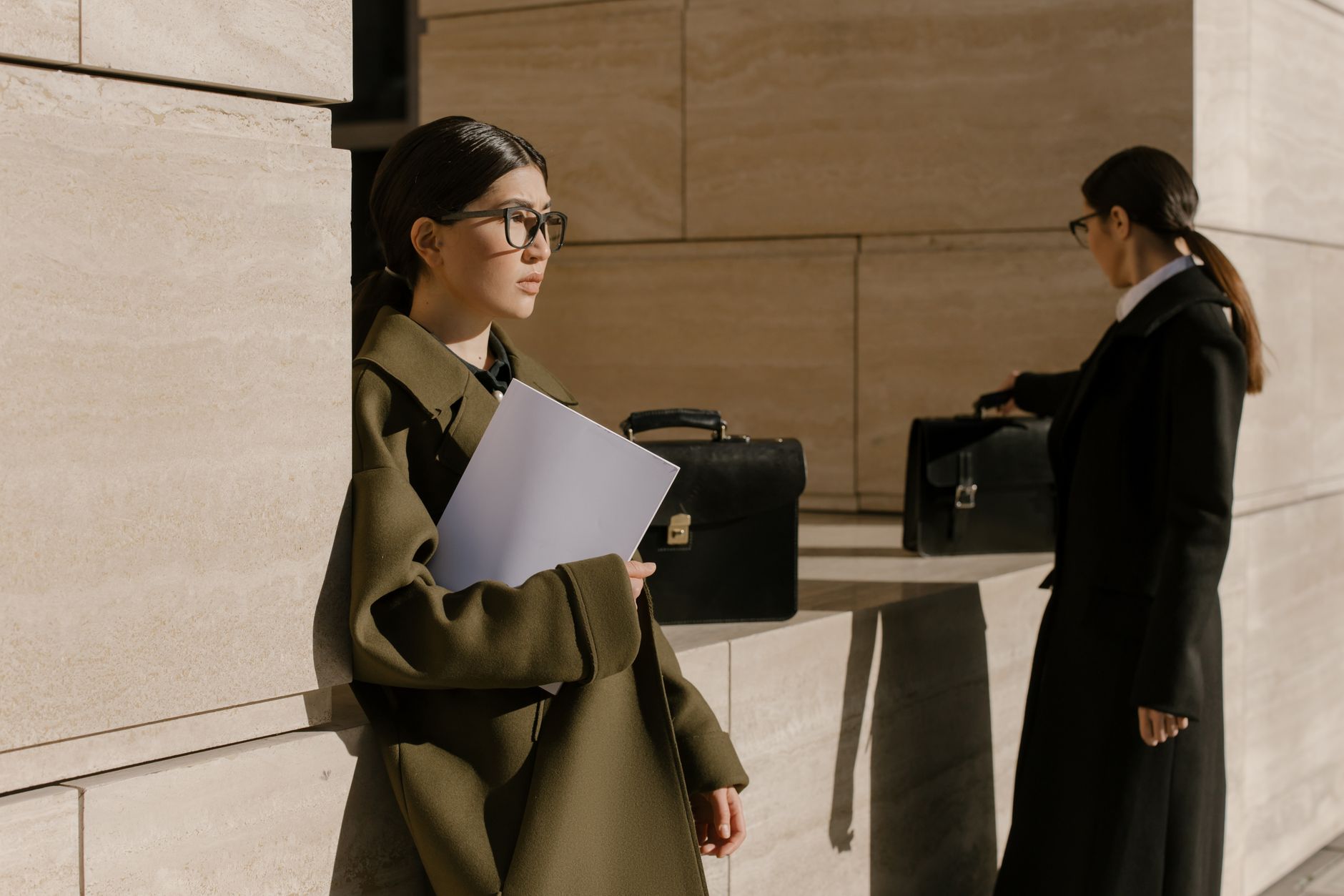 Two women in professional attire with briefcases, outdoors on a sunny day.
