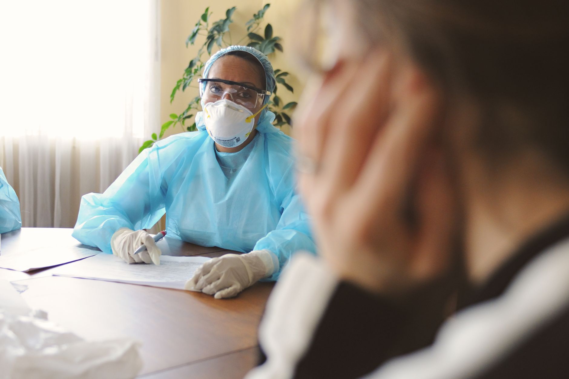 Healthcare professional in protective gear consulting with a patient indoors.