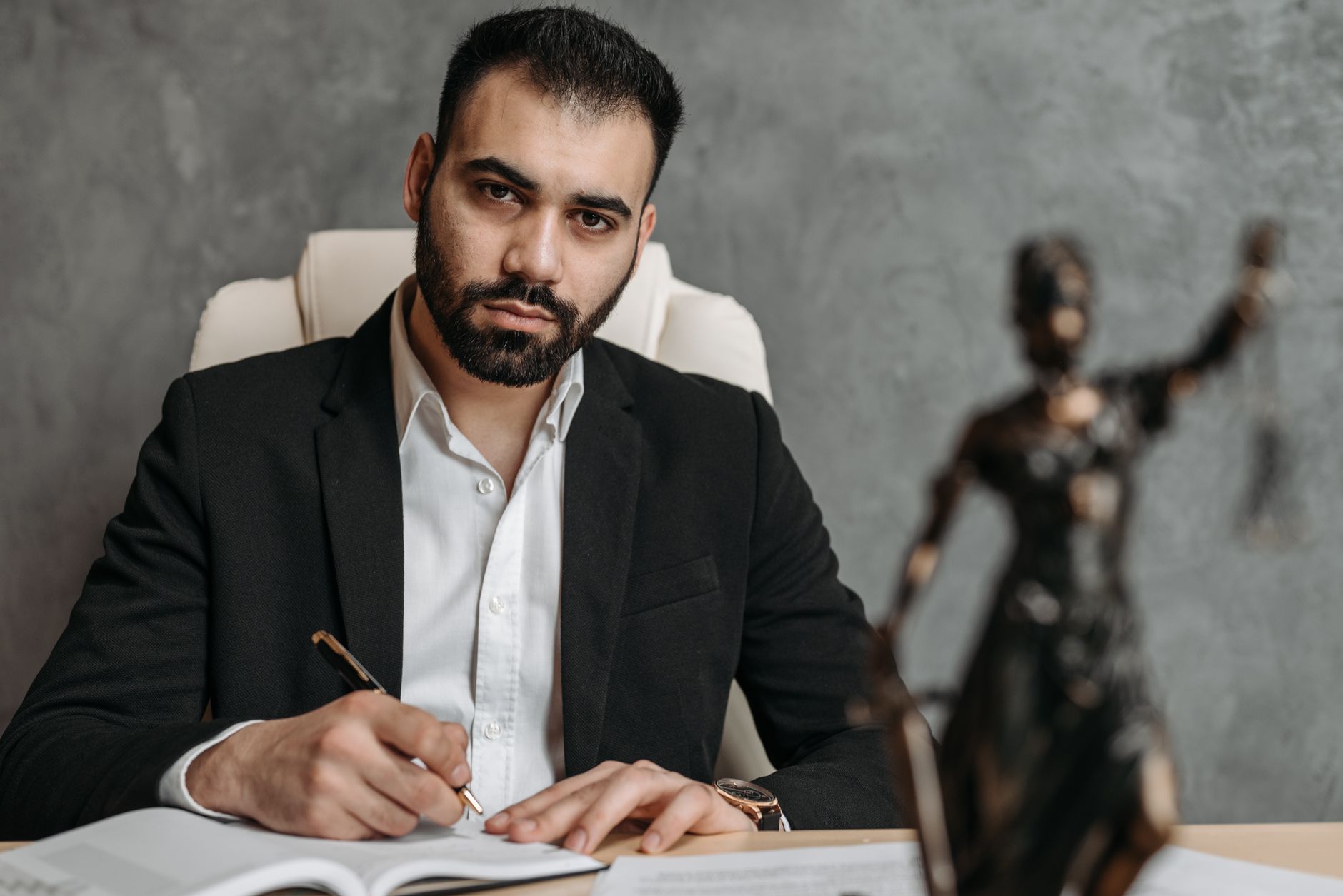 A serious lawyer in a black suit working diligently at his office desk.