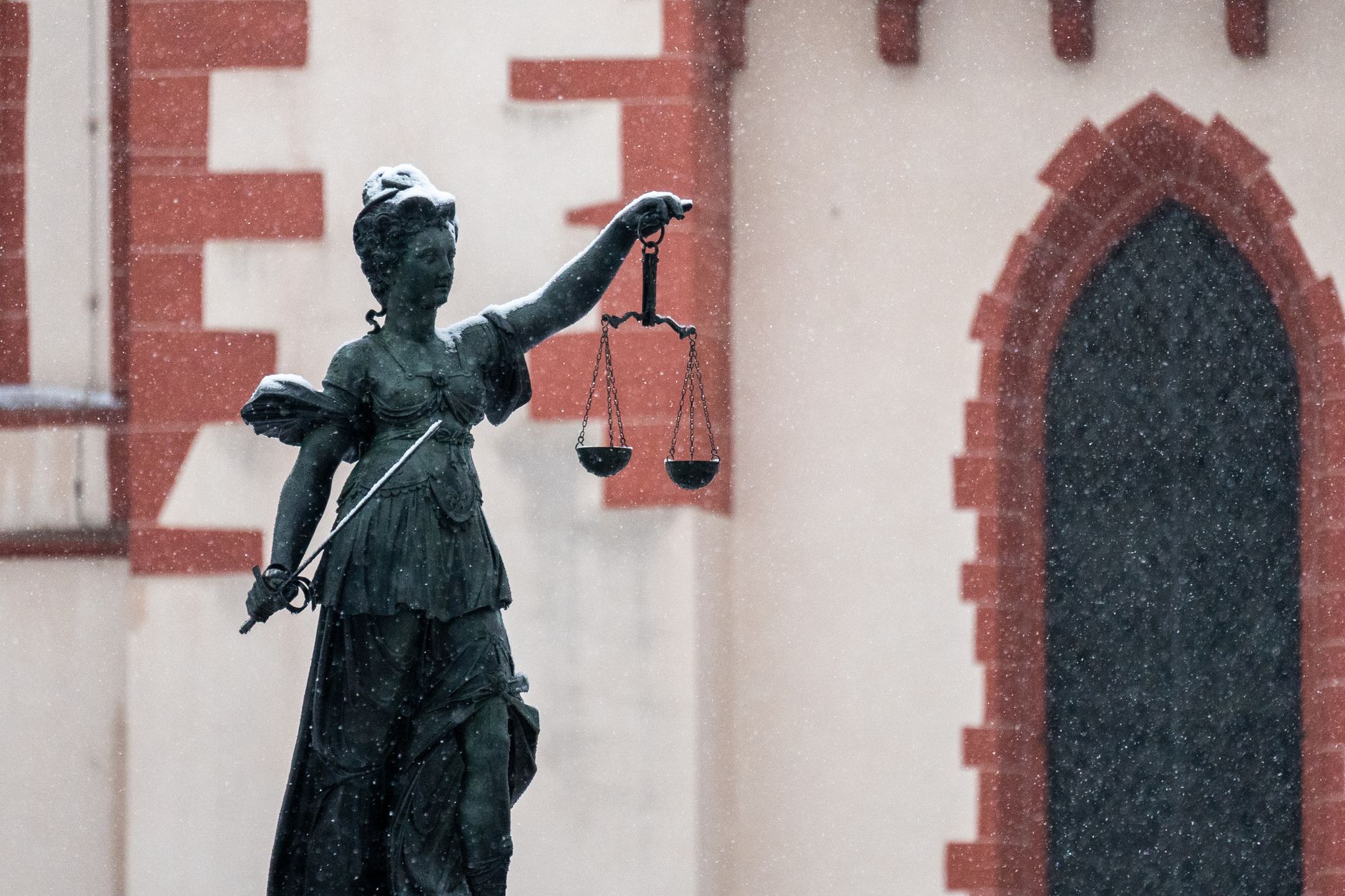A statue of Lady Justice in an urban area during snowfall.