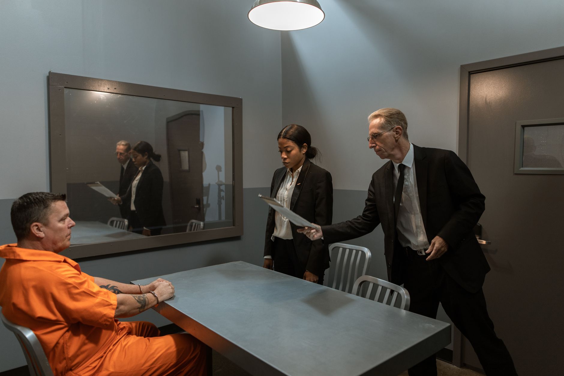 Intense interrogation scene featuring detectives interviewing a prisoner in handcuffs in a dimly lit room.