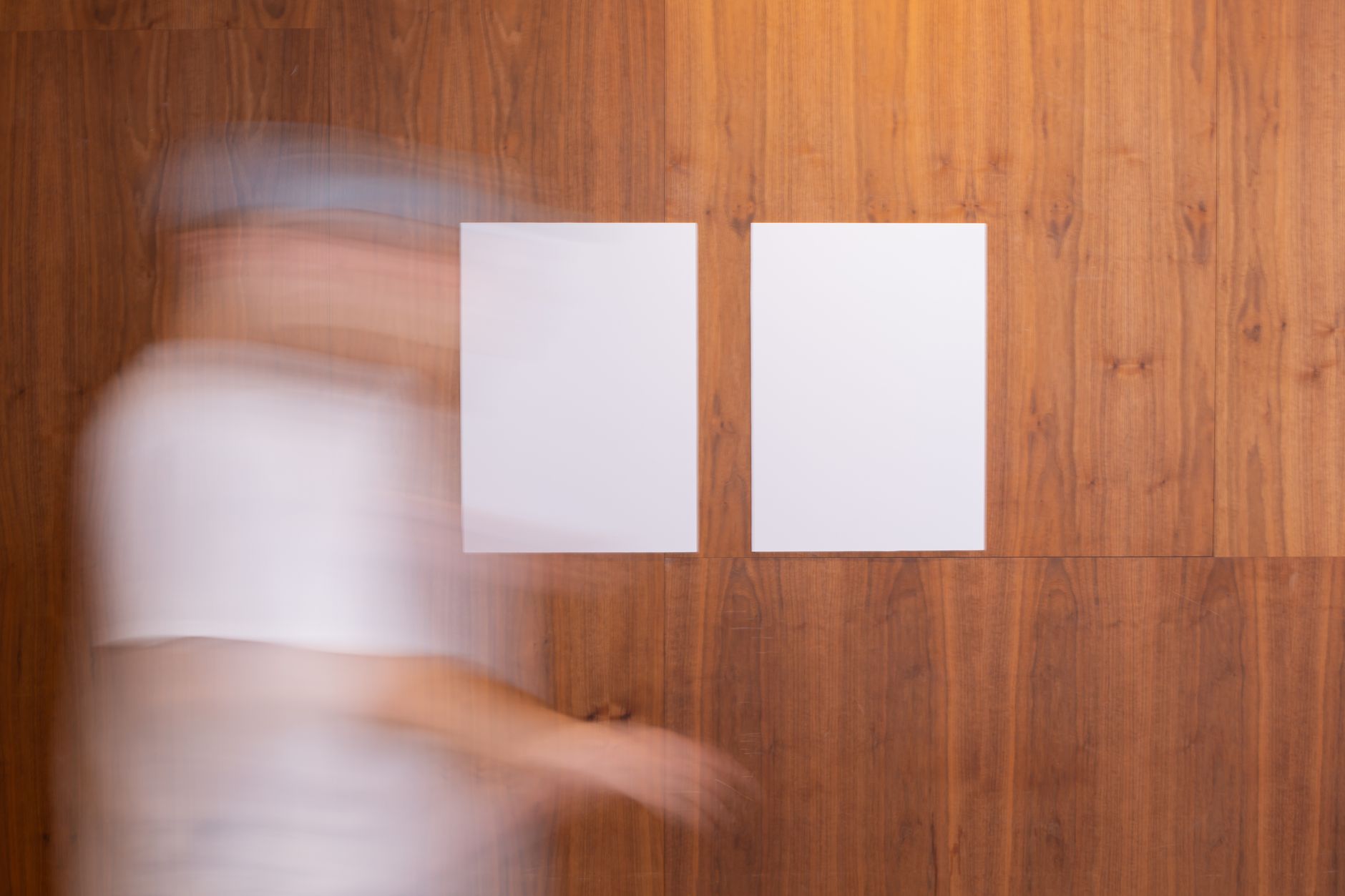 Side view of anonymous blurred person in motion strolling along wooden wall with white mock up posters in light room