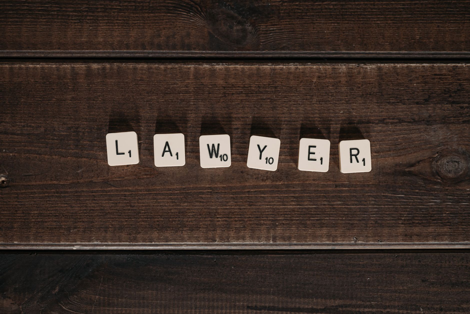 Close-up of scrabble tiles spelling 'lawyer' on a dark wooden surface.