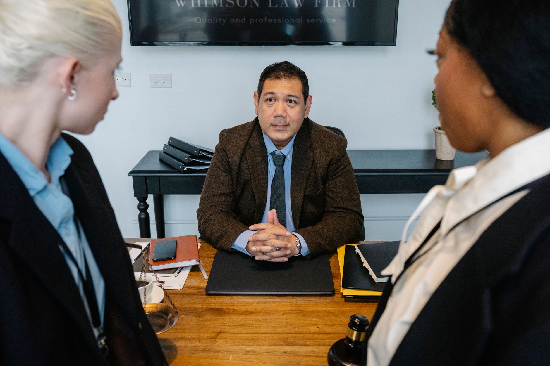 From above of concentrated middle aged ethnic boss discussing strategy with attentive young diverse female colleagues sitting at table in law firm