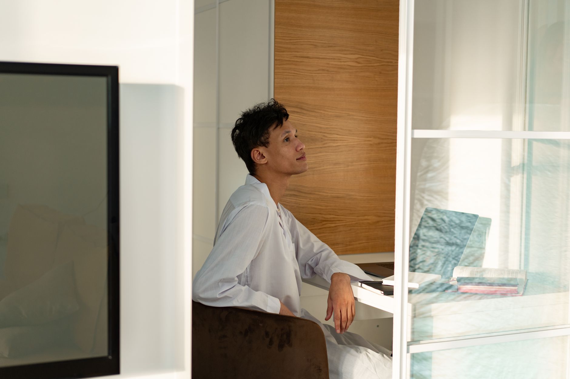An adult man sitting in a bright, modern home office space with a thoughtful expression.