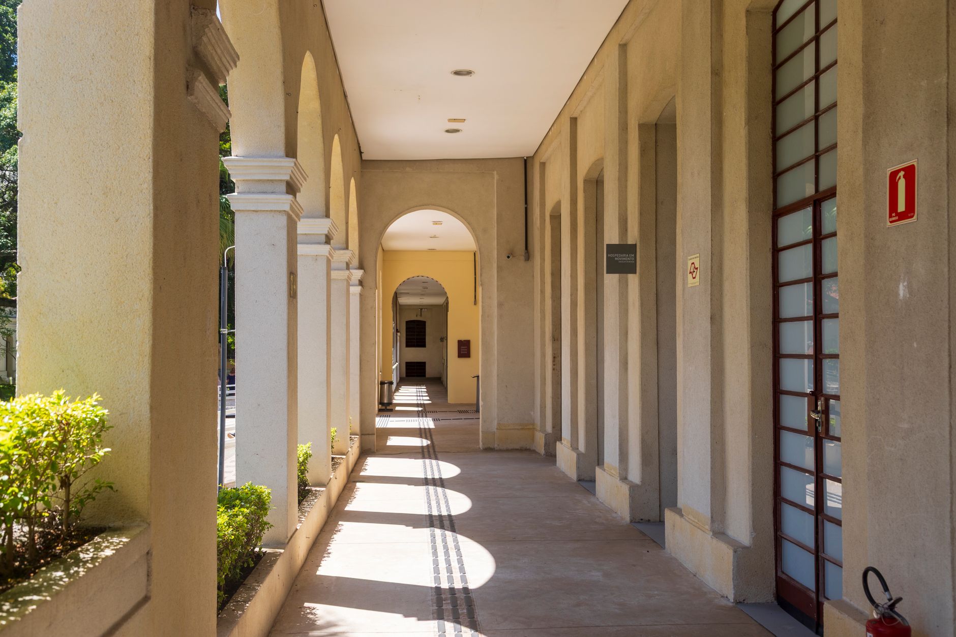 Sunlit corridor with archways casting shadows on a sunny day.