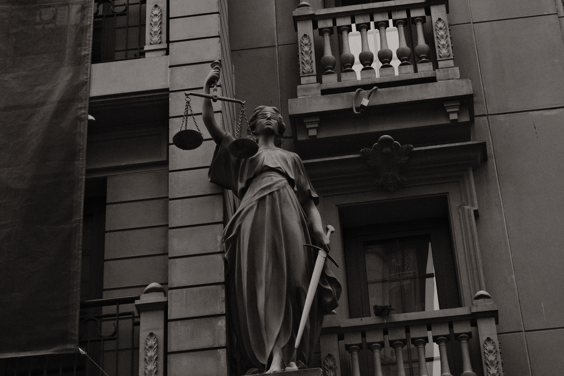 A black and white image of Lady Justice statue against a building facade symbolizing law and fairness.