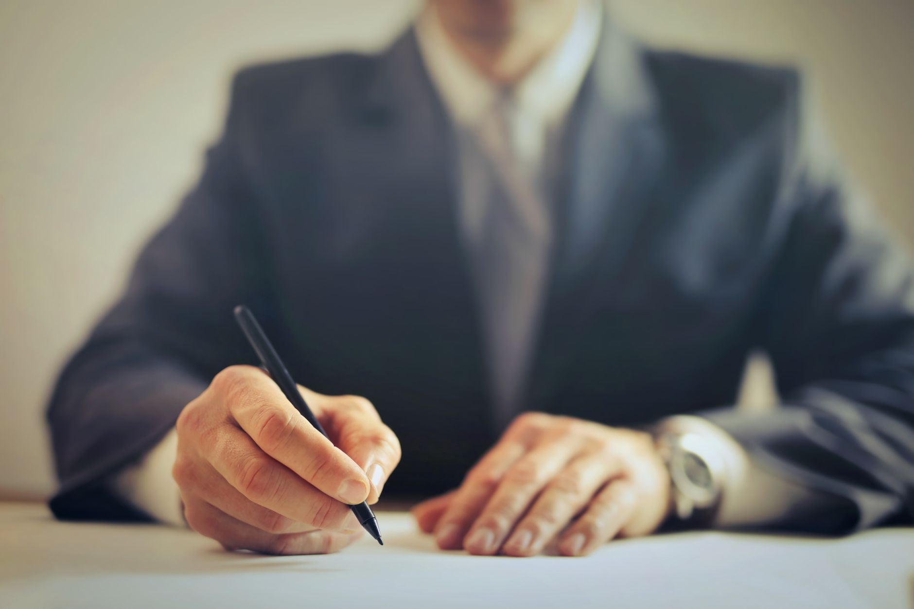 Male entrepreneur wearing formal suit sitting at table in workplace and signing documents while making successful business deal