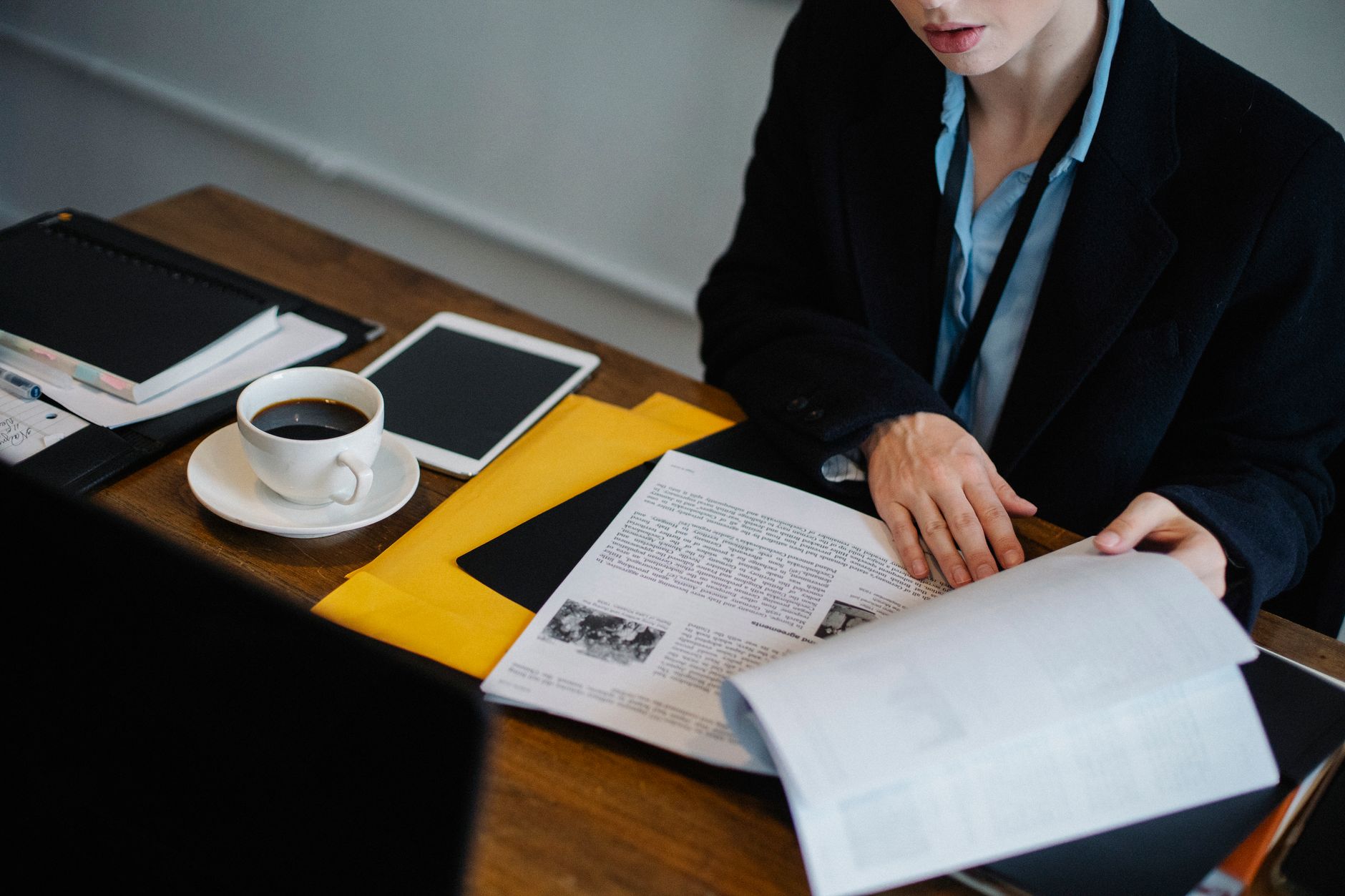 High angle of crop faceless businesswoman in formal clothes sitting at table with tablet and hot coffee and looking through documents