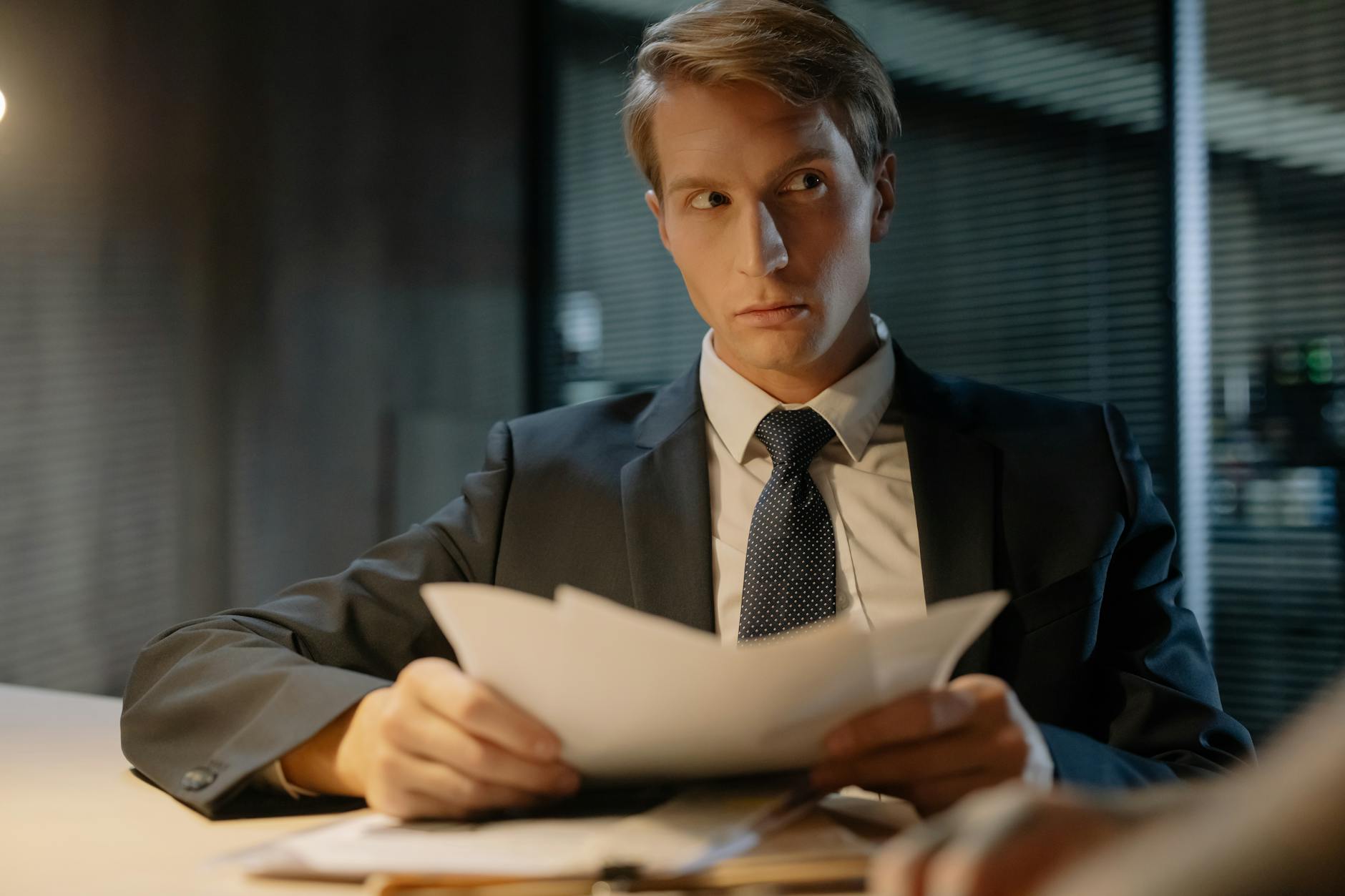 Businessman in suit reviews documents at a desk in a modern office setting.