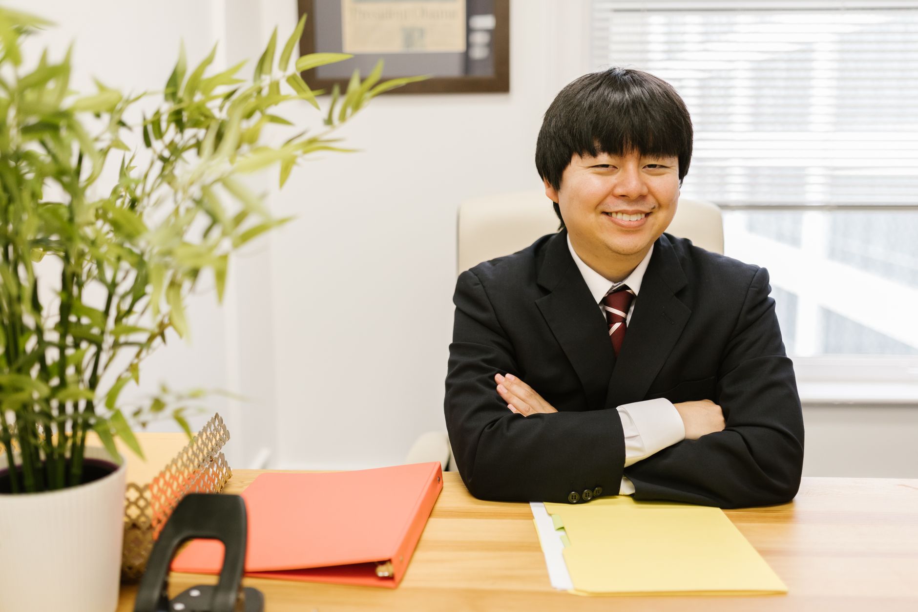 Businessman in suit sitting at desk, smiling confidently in an office environment.