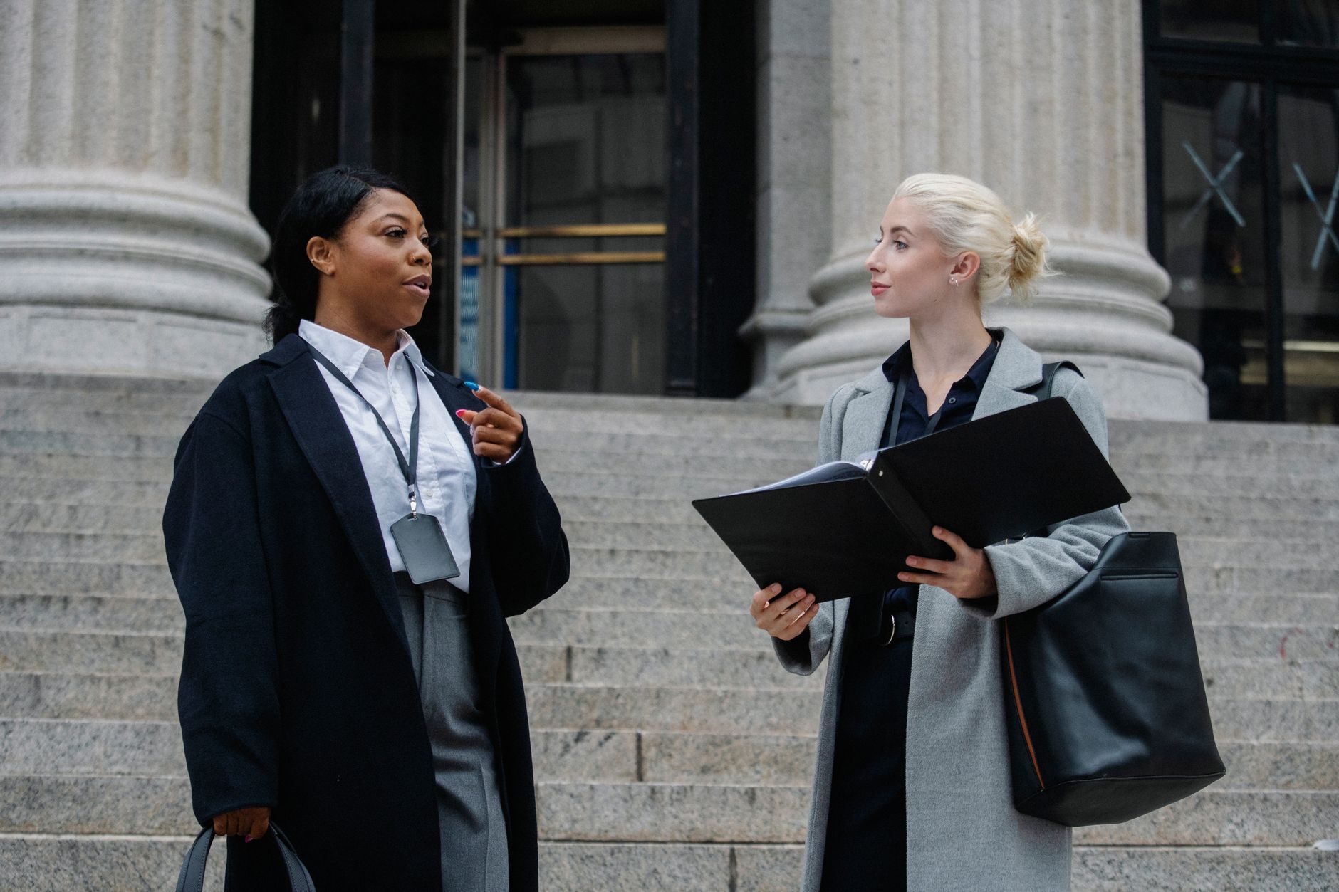 Smart young multiracial female lawyers talking about case standing near aged court building with columns before trial