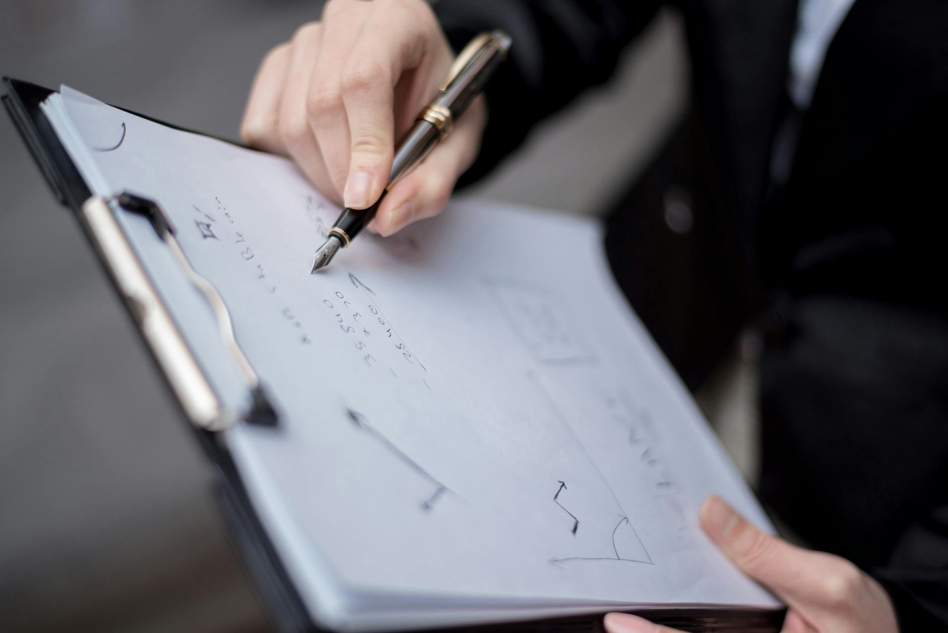 A person writing on a clipboard using a pen, focusing on the hand and paper.