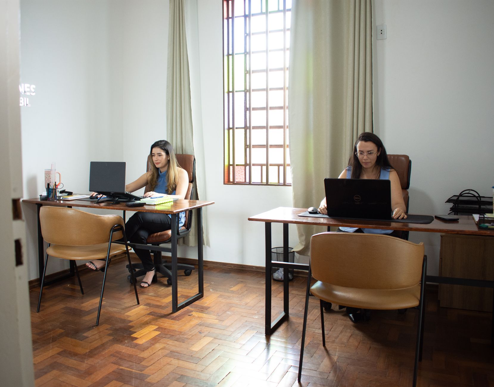 Two women working on laptops in a well-lit office in Tiros, Minas Gerais, Brazil.