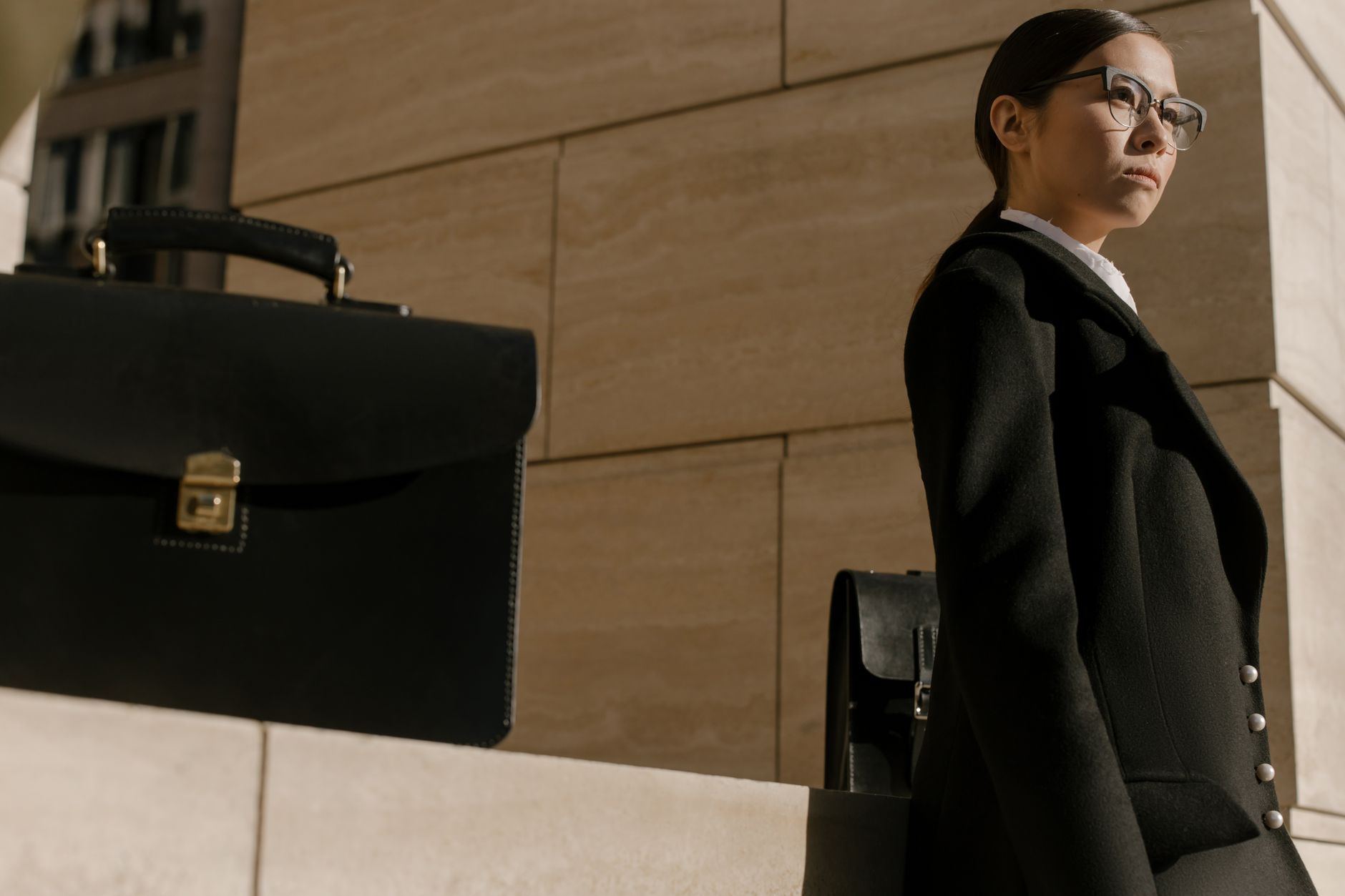 Confident businesswoman in professional attire standing by an office building with a briefcase.
