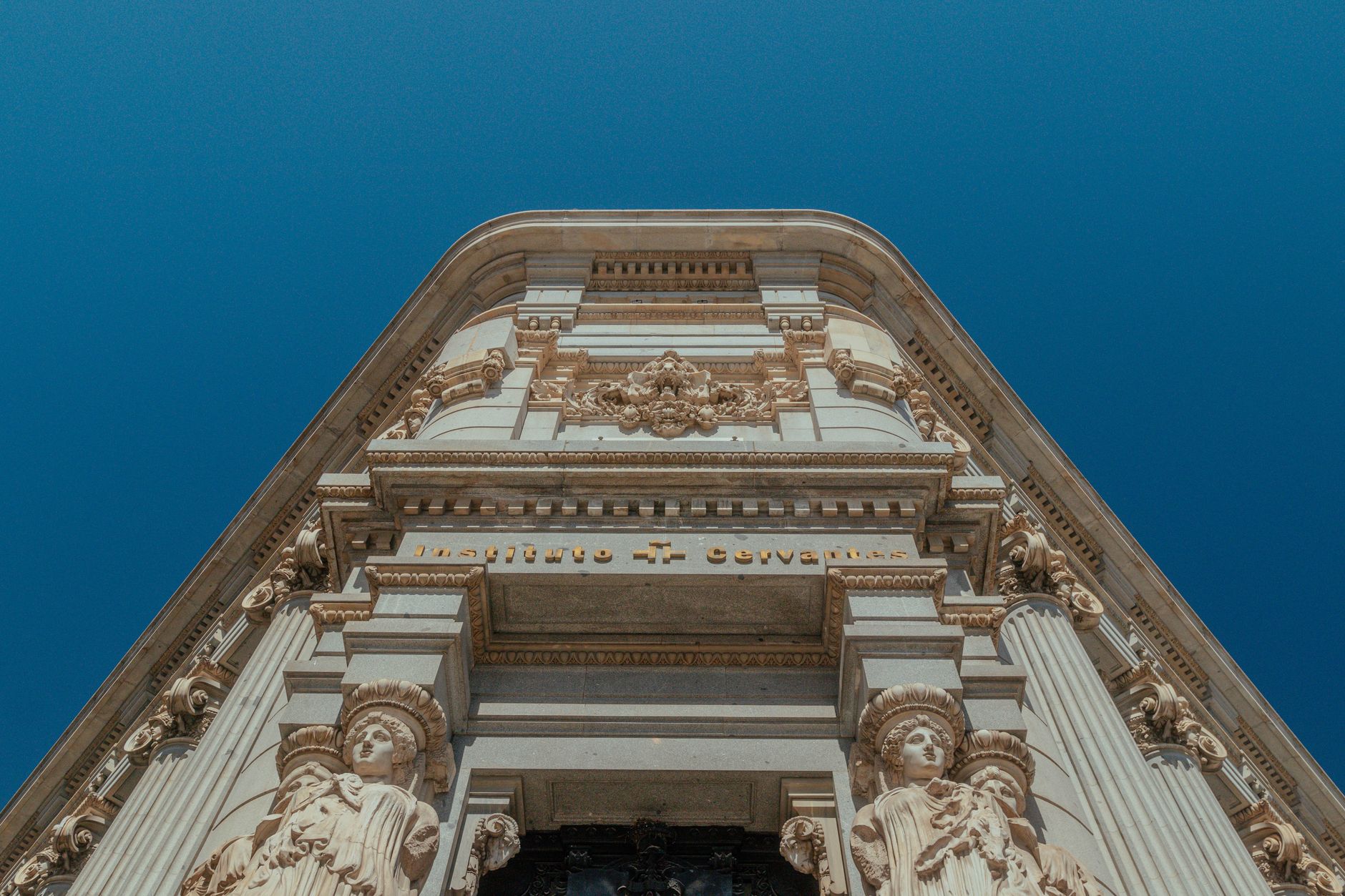 Ornate architecture of Instituto Cervantes with sculptures, set against a clear blue sky.