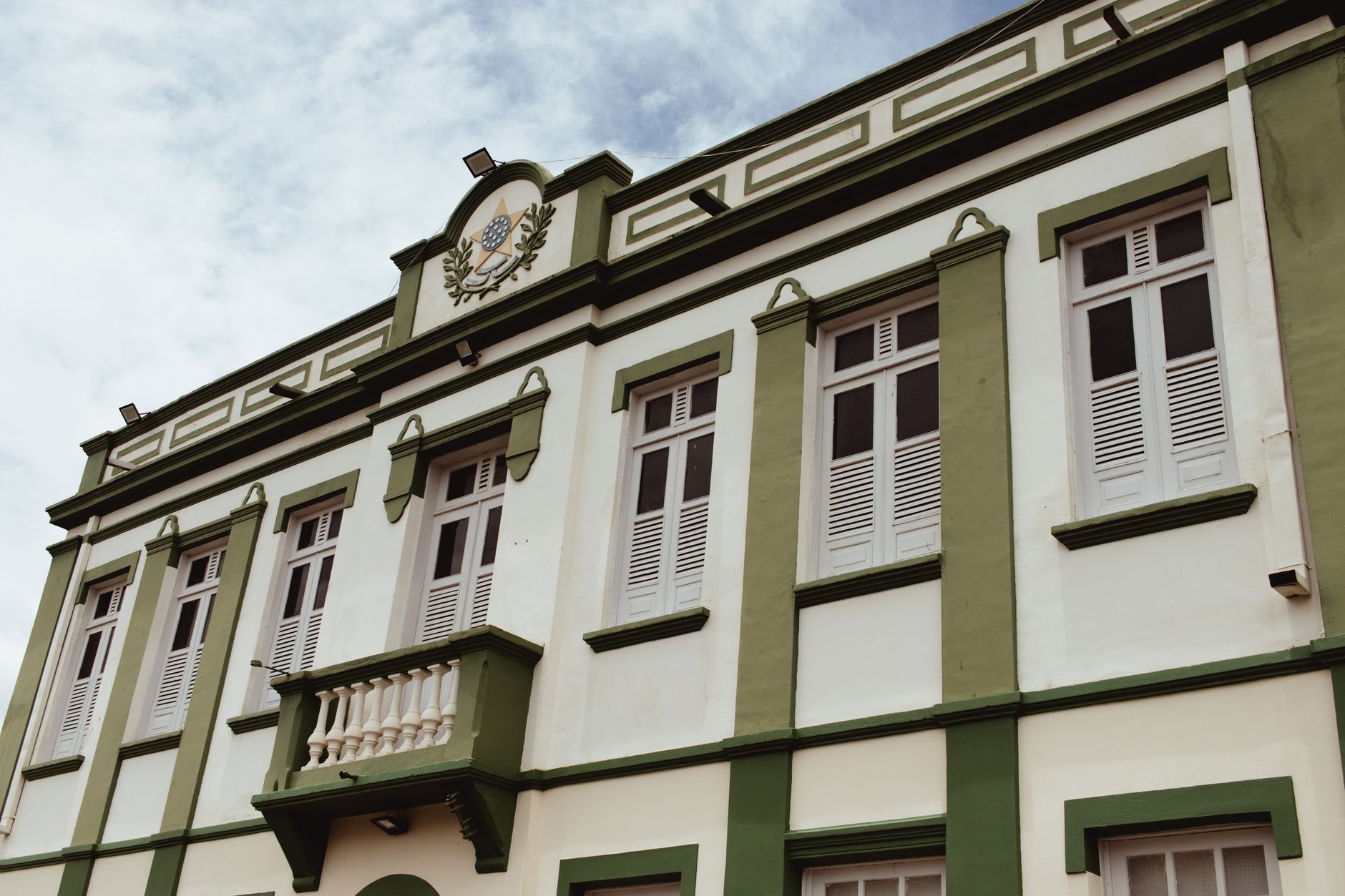 Low angle view of a classic building with ornate green facade and shuttered windows under a clear sky.
