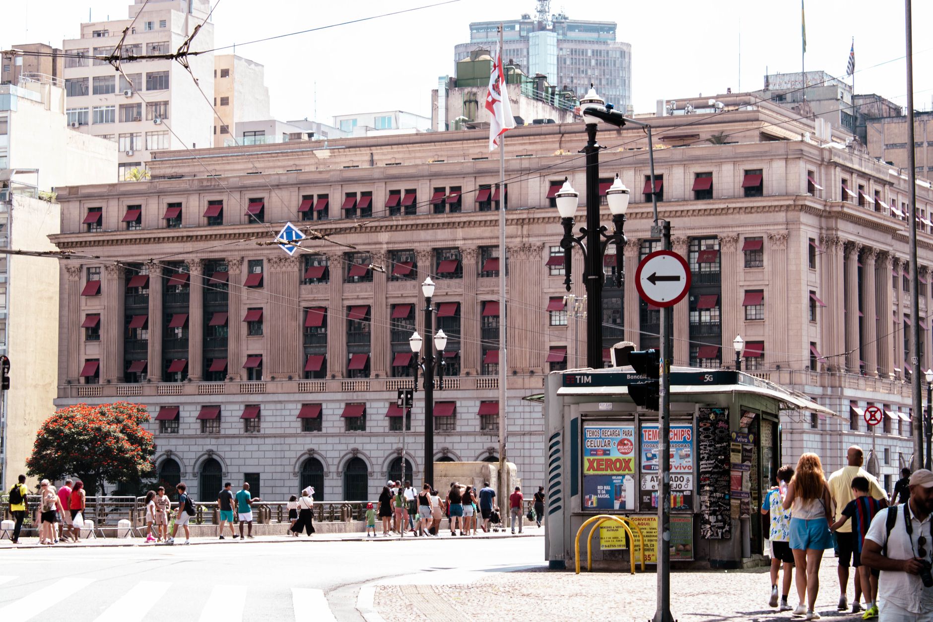 Crowd and traffic in front of a historic building in São Paulo, Brazil, on a sunny day.