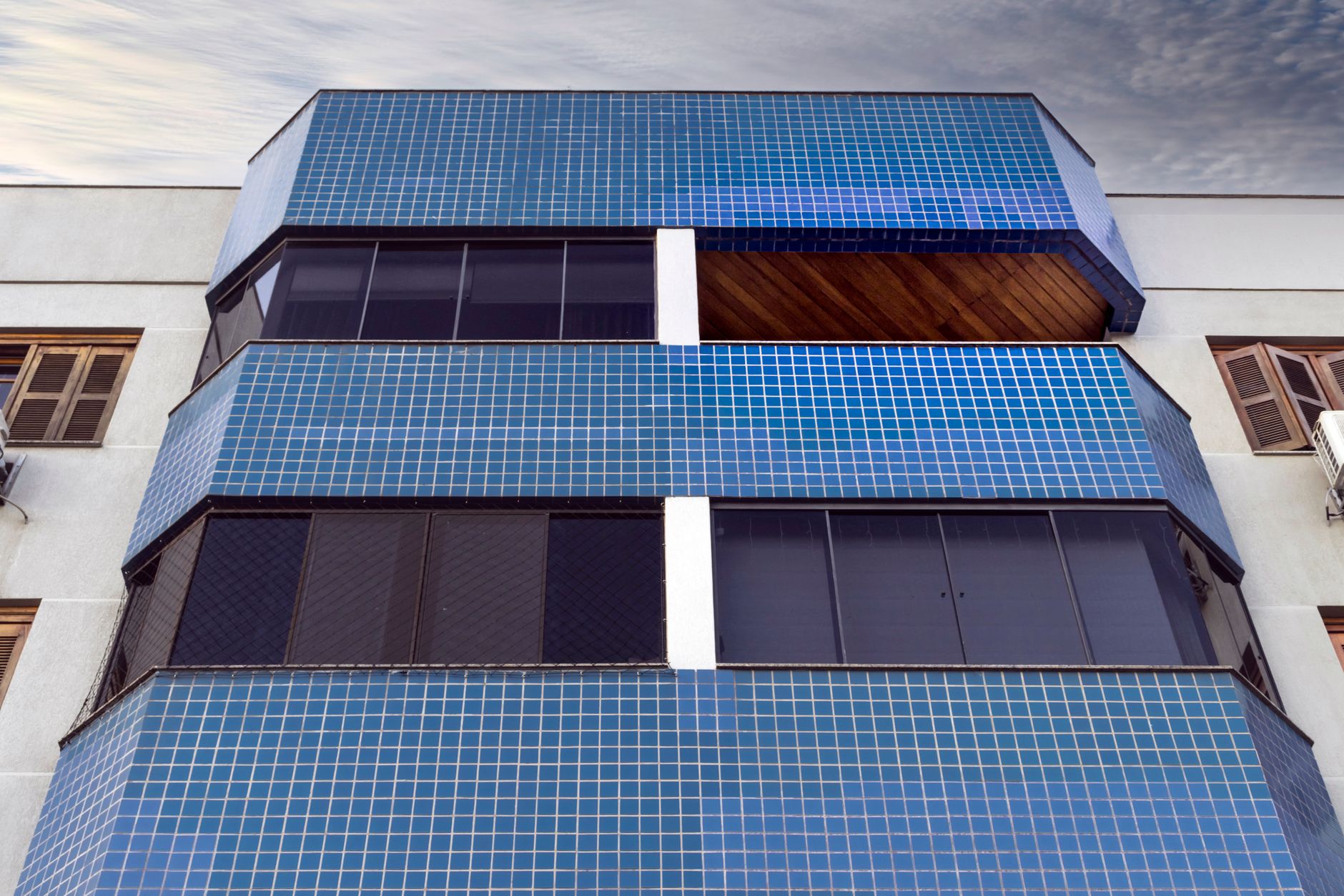 Close-up of a modern building facade with blue tiles and glass windows under a cloudy sky.