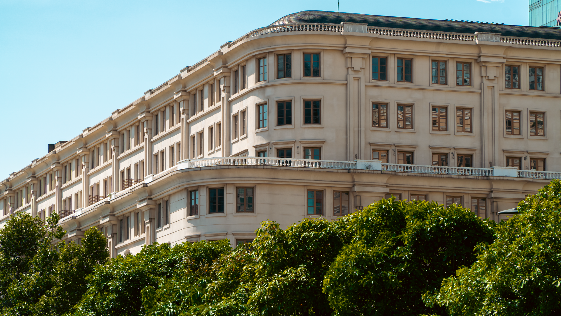 Elegant historic building facade surrounded by lush greenery under bright daylight.