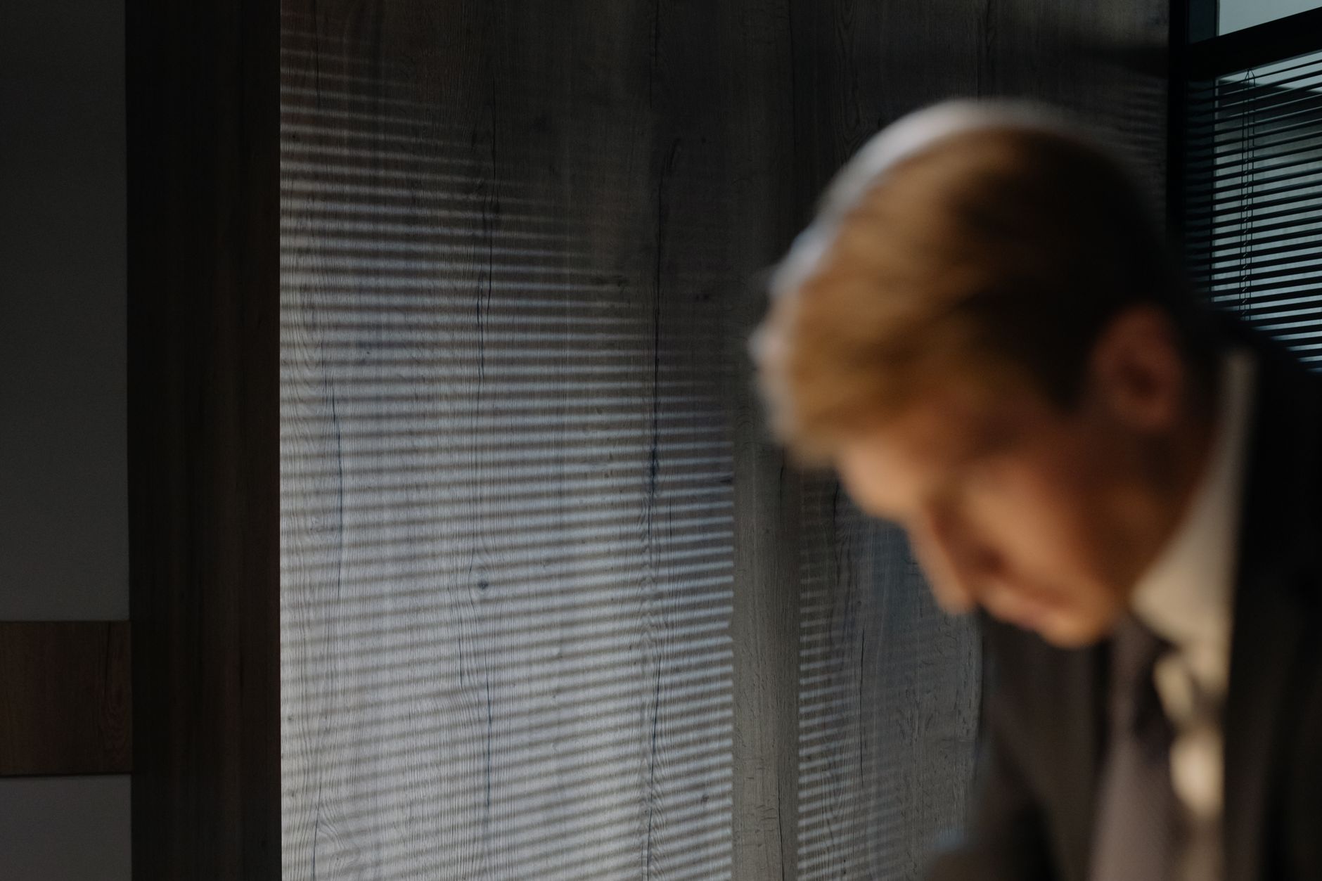 Blurred image of businessman in suit against wall with shadow lines and soft light.