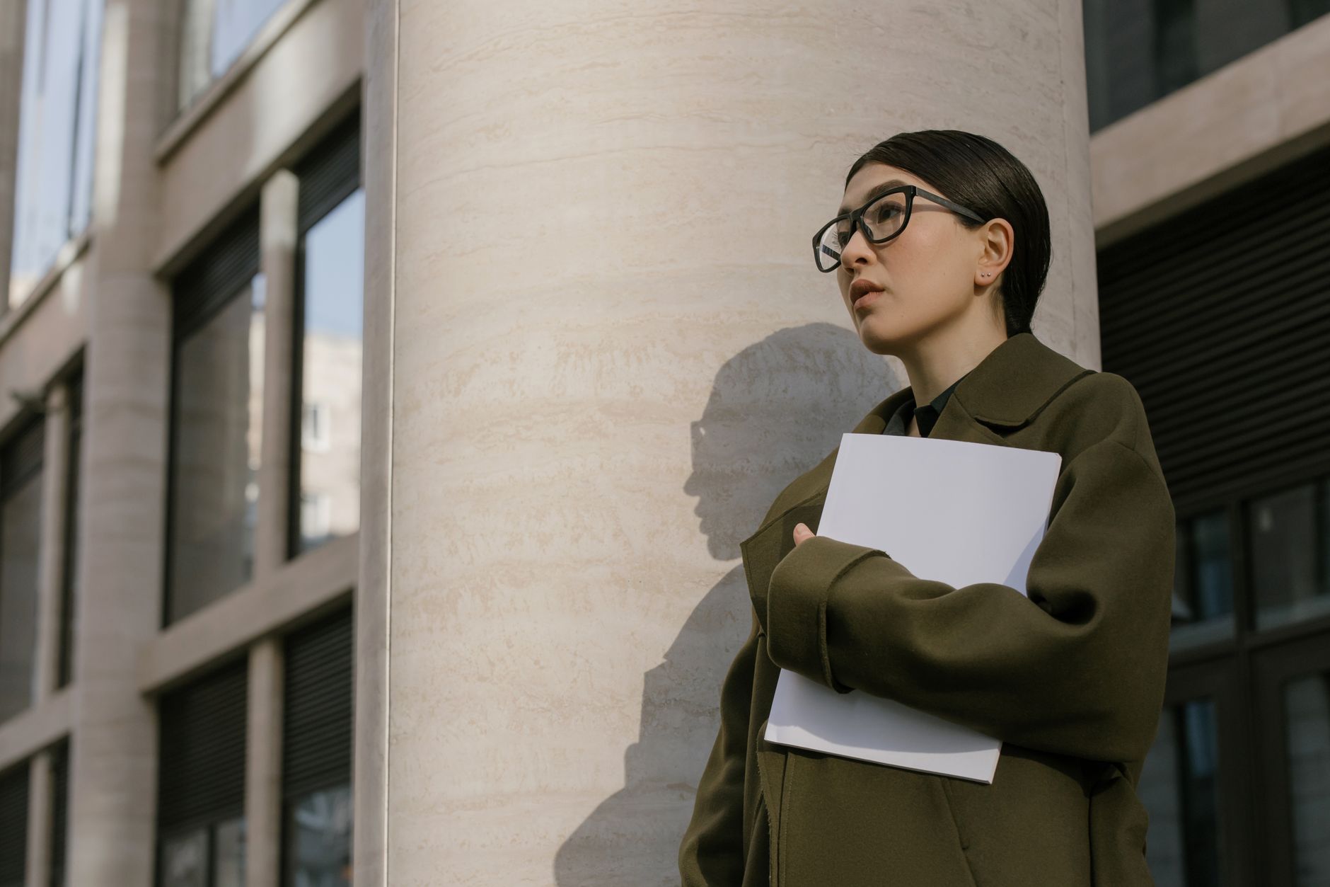 Businesswoman in coat holds documents against urban building, exuding professionalism.
