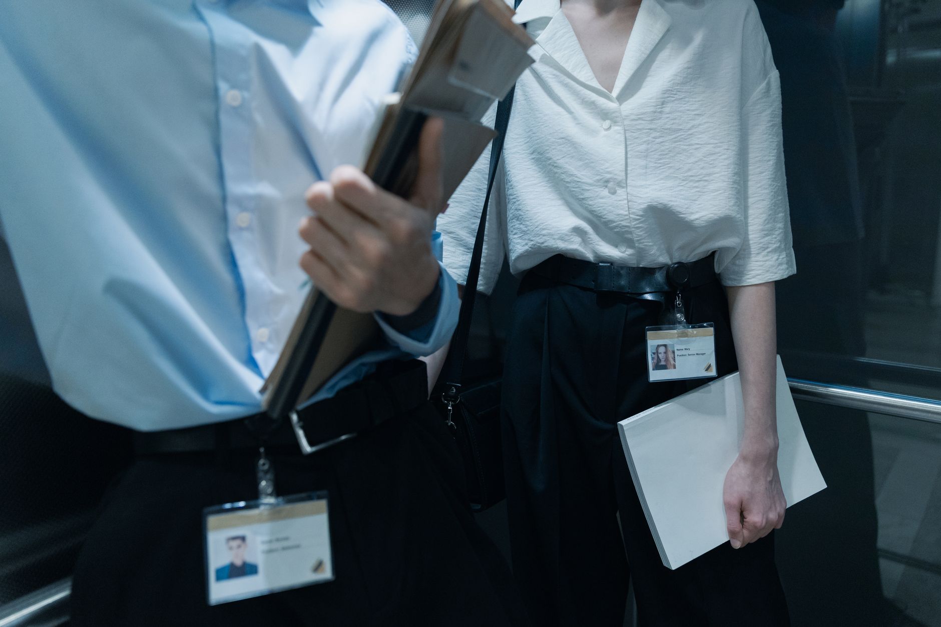 Two professionals in an elevator carrying documents, showcasing office attire.