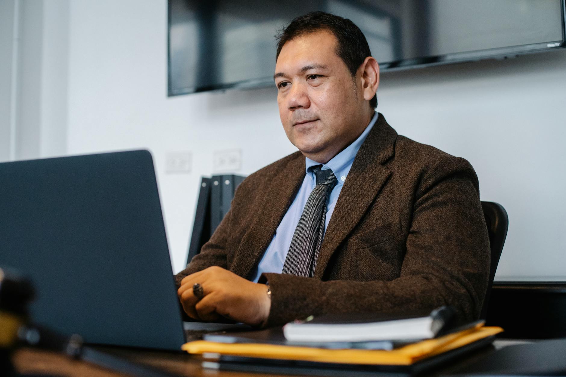 Serious ethnic mature male entrepreneur in classy suit and tie working on laptop while sitting at desk in modern office