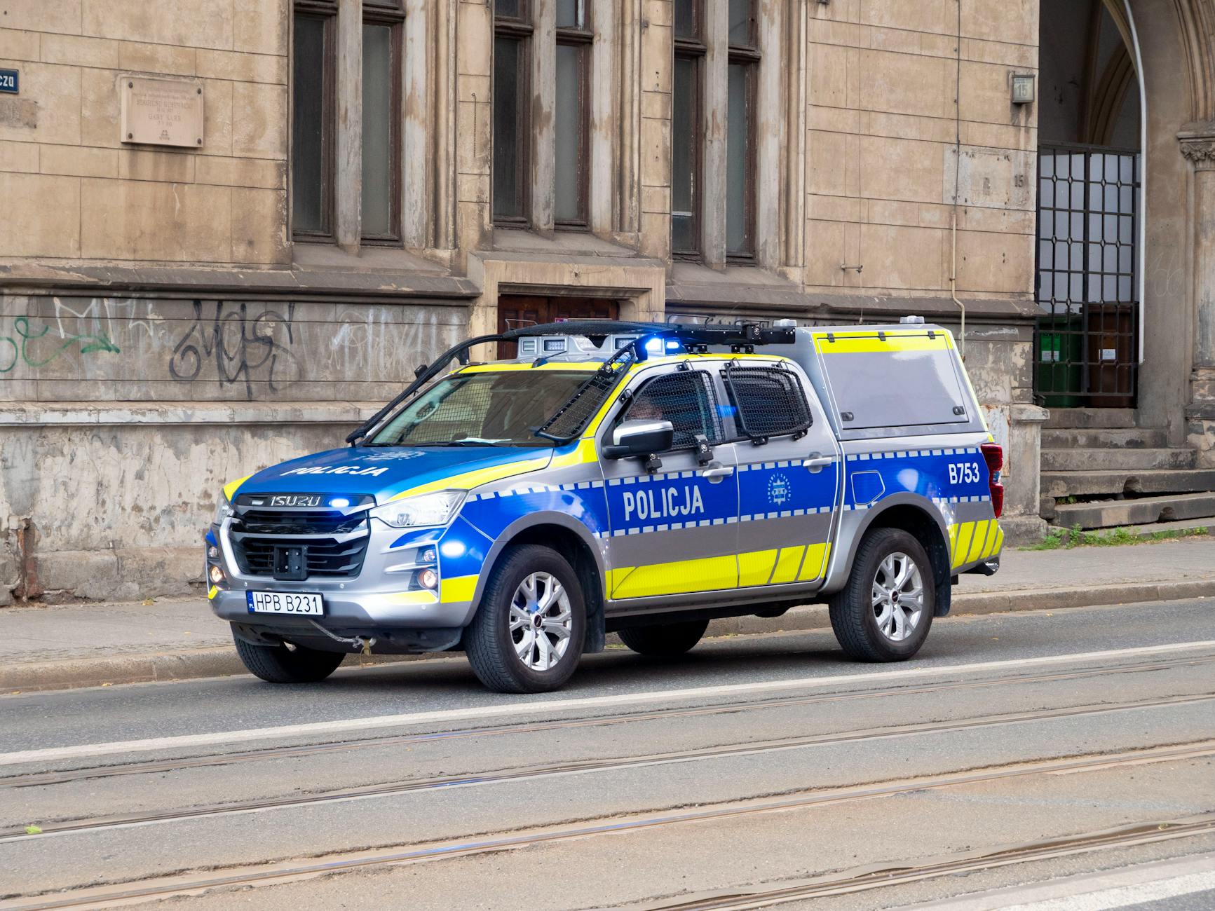 Blue and yellow police car parked on the street in Wrocław, Poland, beside an old building.