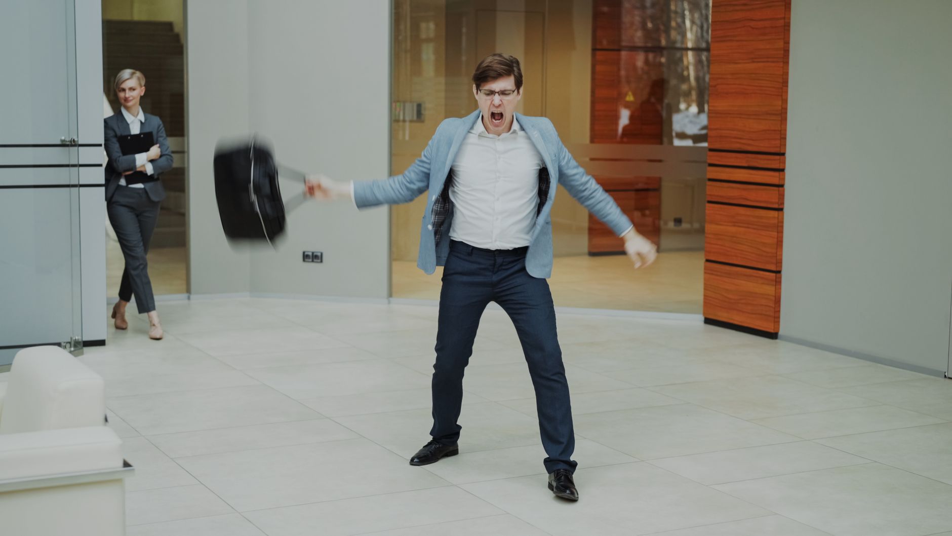A businessman expresses frustration by throwing his briefcase inside a modern office setting.