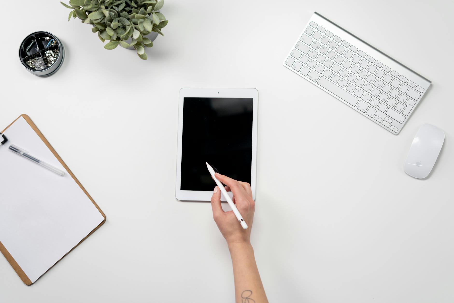 A clean workspace featuring a tablet, keyboard, and mouse on a white desk.