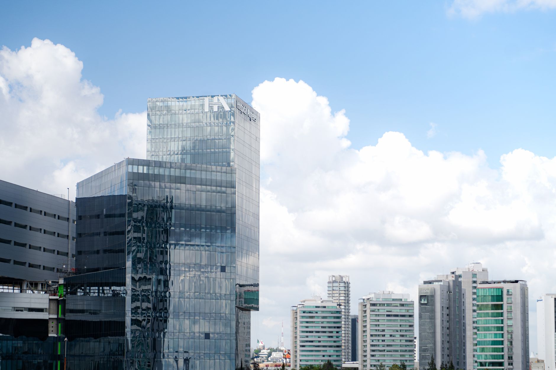 Panoramic view of sleek, glass skyscrapers with blue sky and clouds.