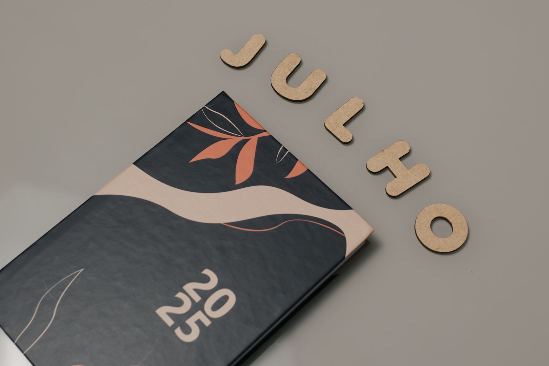 Stylish 2025 planner on a neutral surface with 'Julho' spelled in wooden letters.