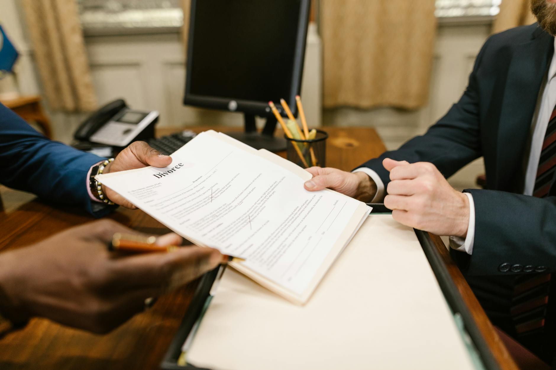 Close-up of hands exchanging divorce documents during legal proceedings in office.