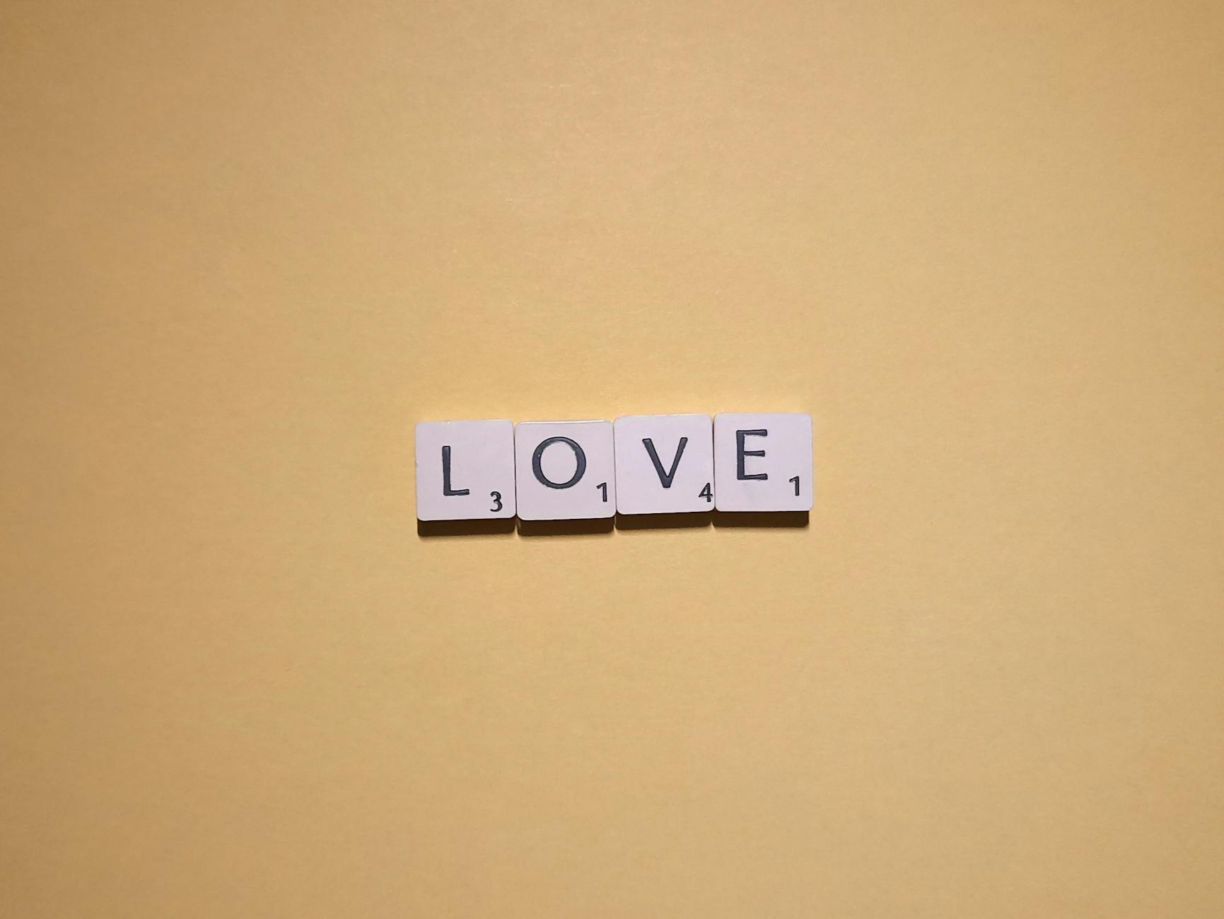 Scrabble tiles spelling 'LOVE' on a warm yellow background, minimalist design.
