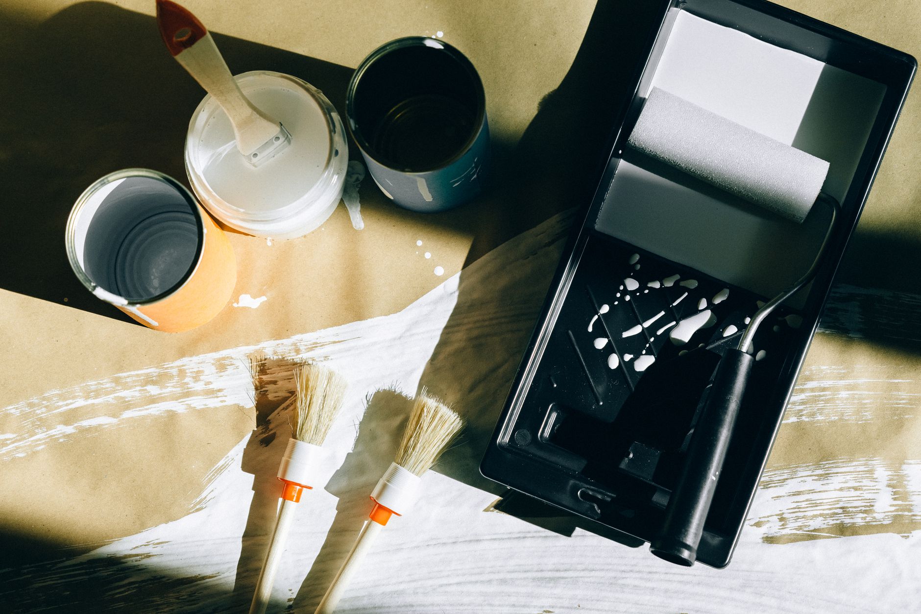 Top view of painting tools including brushes, rollers, and paint cans on paper.