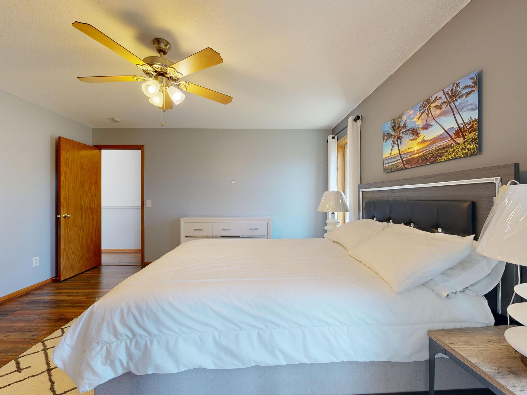 A spacious bedroom featuring a ceiling fan, bed, and wall art with a beach theme.