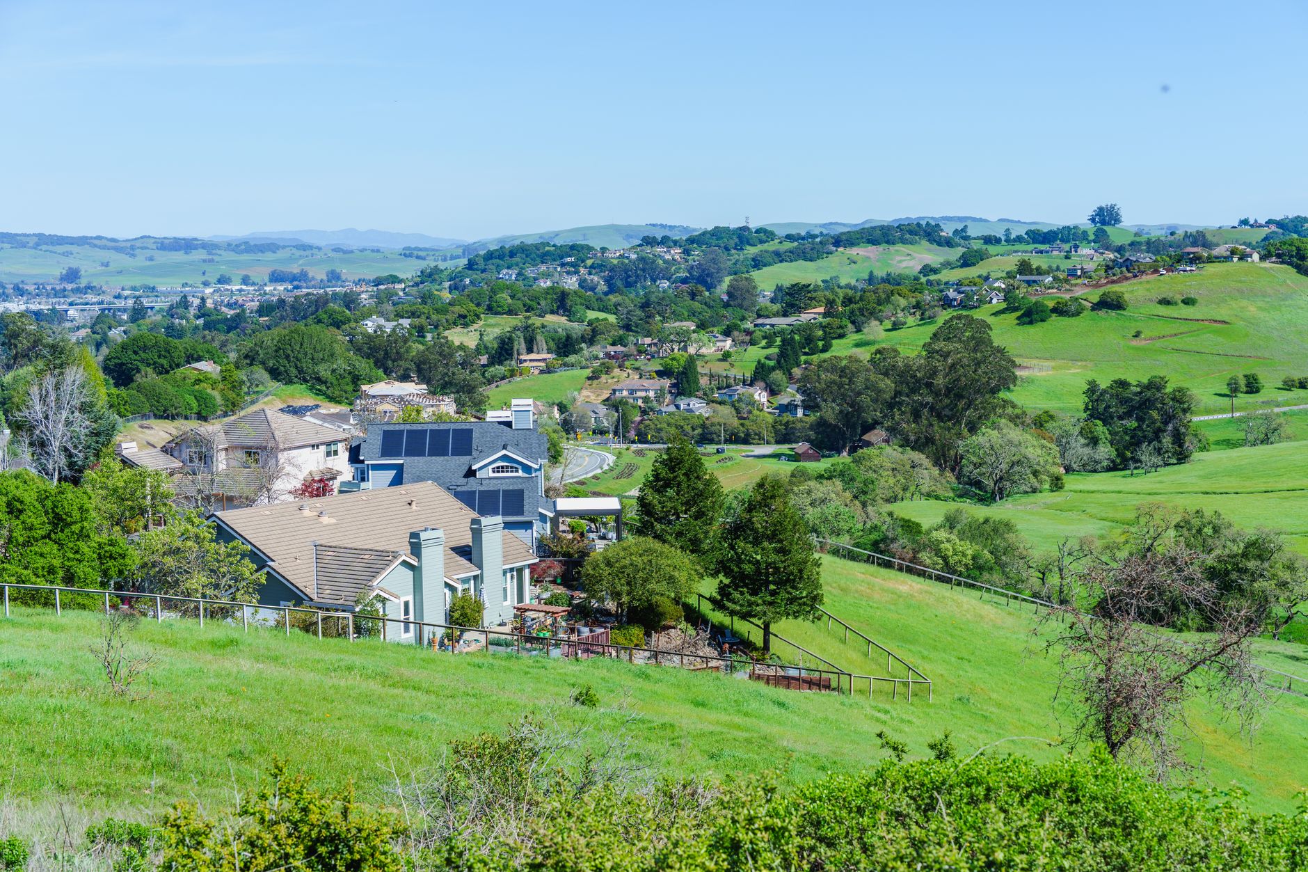 Picturesque suburban neighborhood with lush green hills and clear blue skies, showcasing a peaceful, idyllic lifestyle.