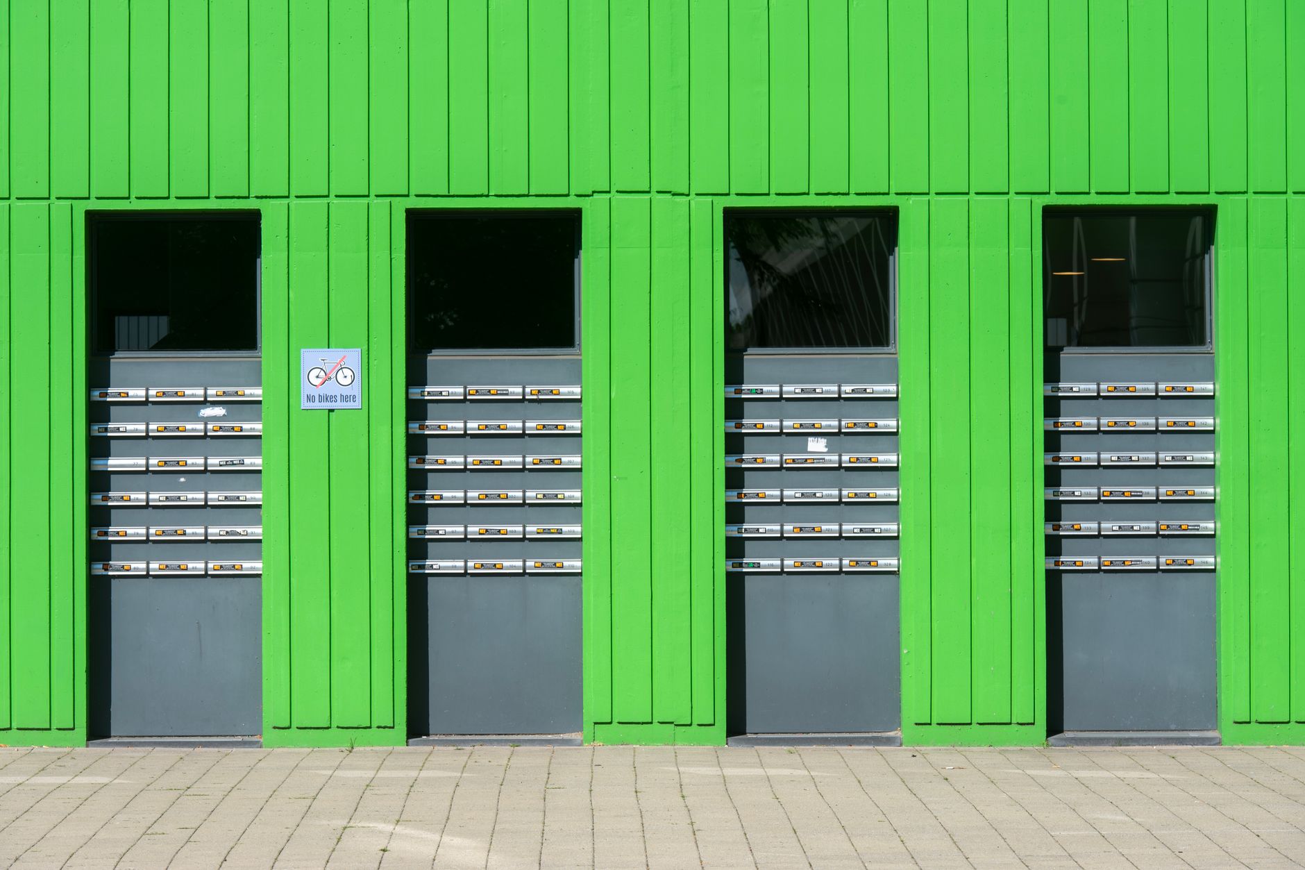 Colorful green facade featuring rows of metallic mailboxes and a no-bikes sign.