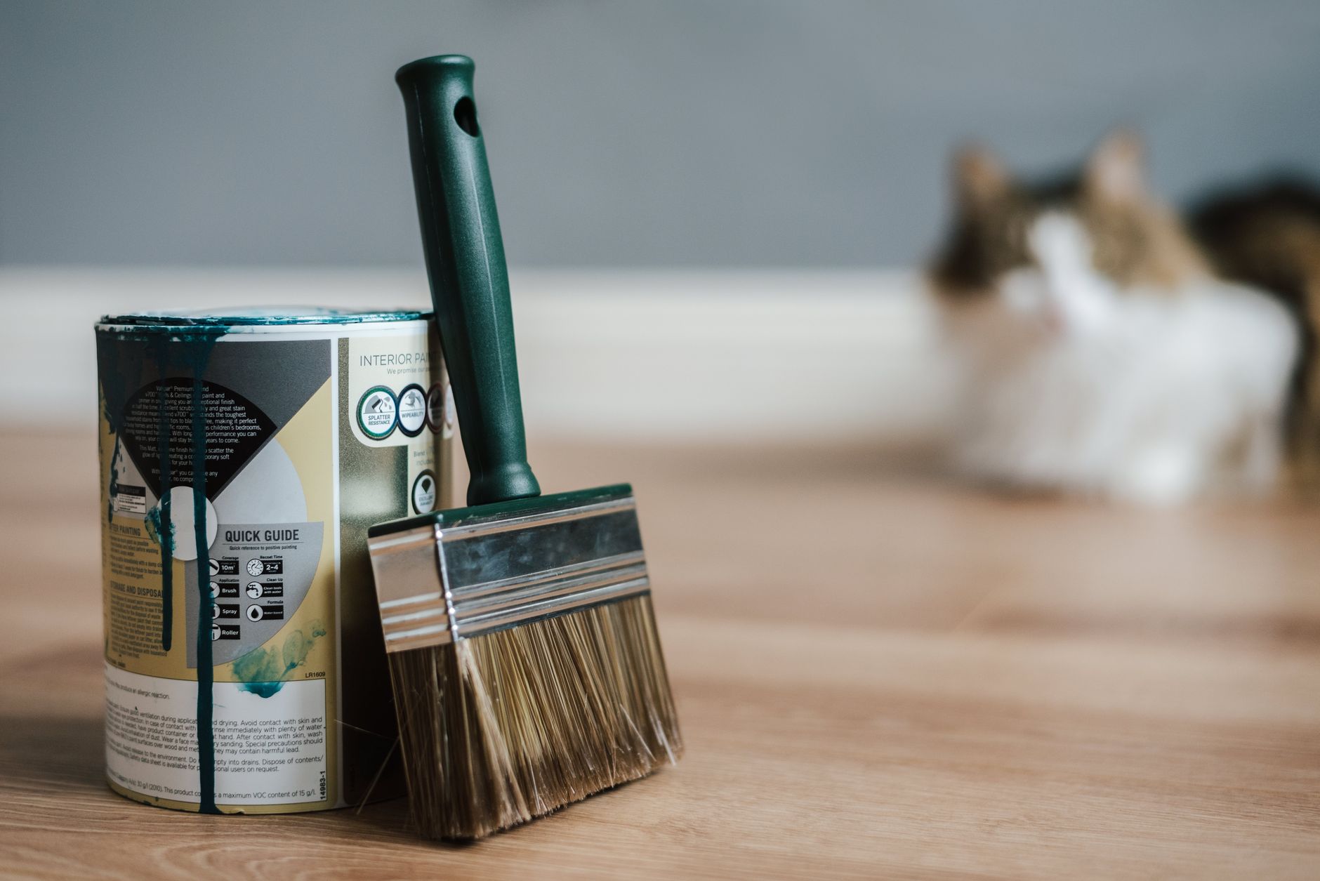 Professional paint brush near metal can with information and dirty flows on parquet in house
